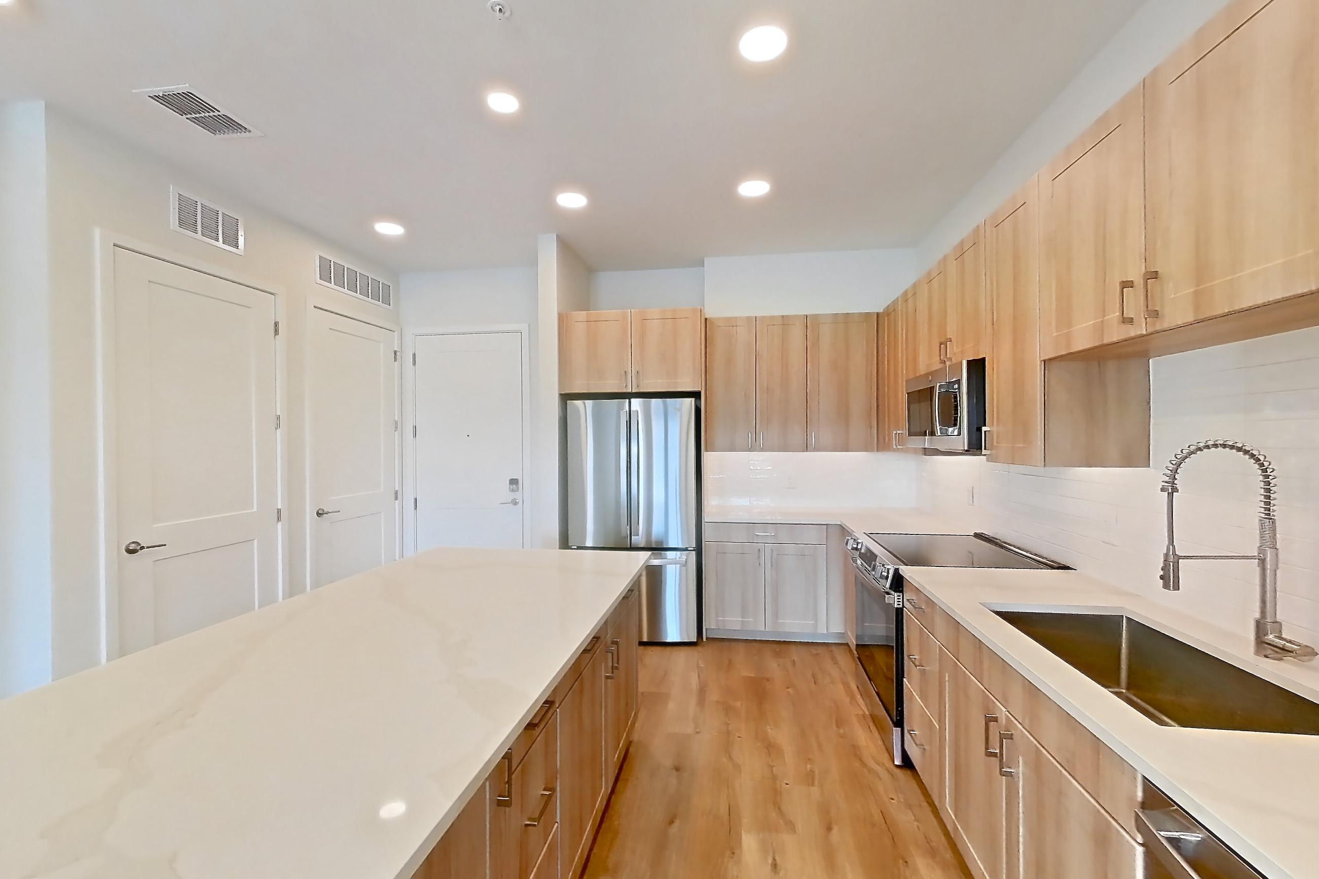 Kitchen with dishwasher, electric range, light countertops, light stone countertops, light wood-finish flooring, microwave, oven/range, refrigerator, and stainless steel appliances, Apartment 251 at Lantower Bayside