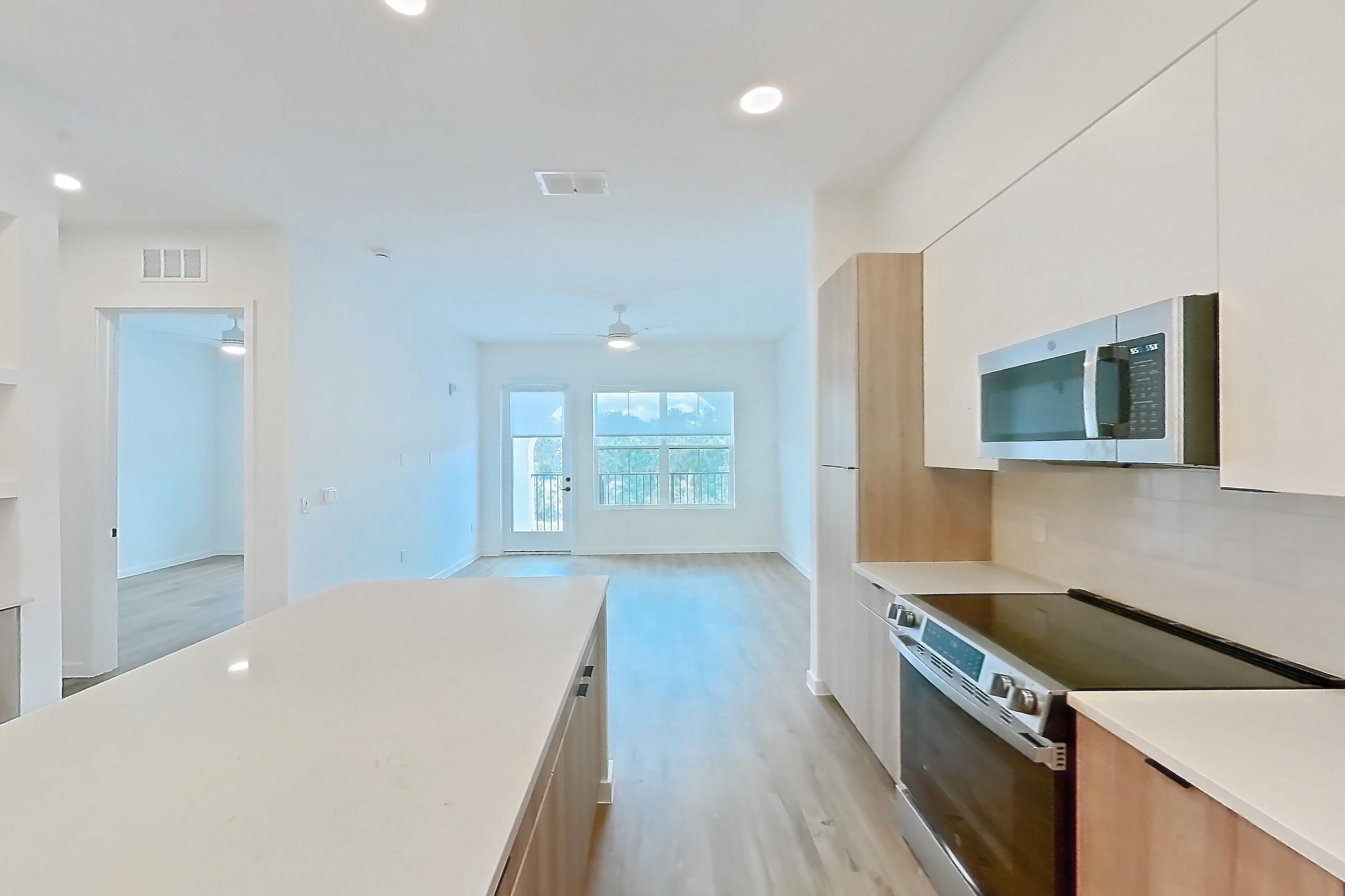 Kitchen with electric range, light countertops, light stone countertops, light wood-finish flooring, microwave, oven/range, refrigerator, and stainless steel appliances, Apartment 240 at Lantower Sunrise