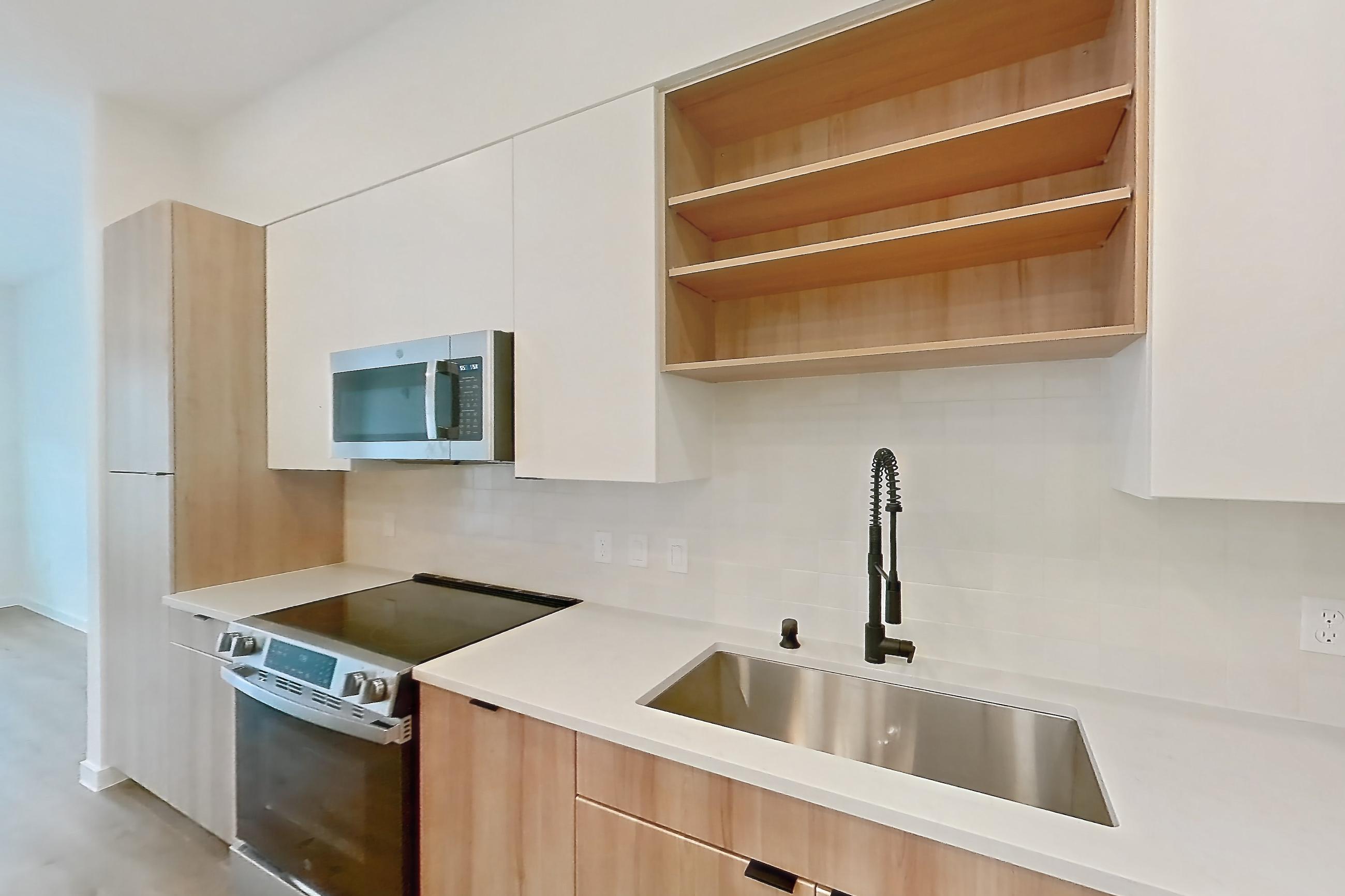 Kitchen with electric range, light countertops, light stone countertops, light wood-finish flooring, microwave, oven/range, refrigerator, and stainless steel appliances, Apartment 240 at Lantower Sunrise
