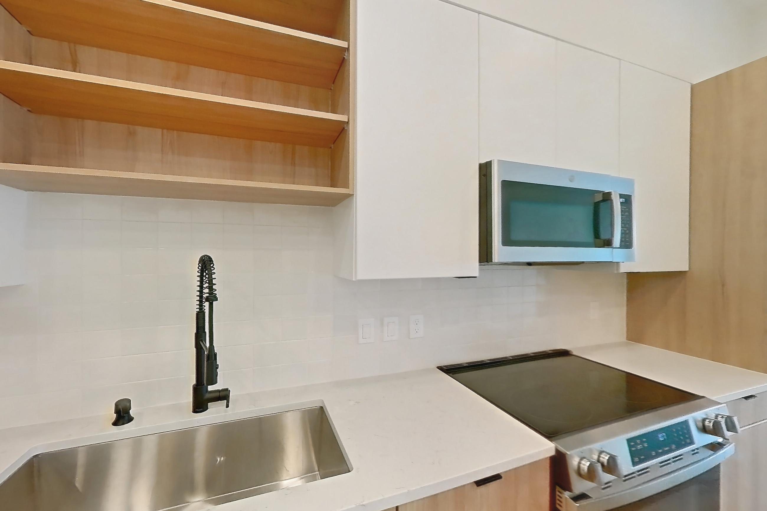 Kitchen with electric range, light countertops, light stone countertops, light wood-finish flooring, microwave, oven/range, refrigerator, and stainless steel appliances, Apartment 338 at Lantower Sunrise