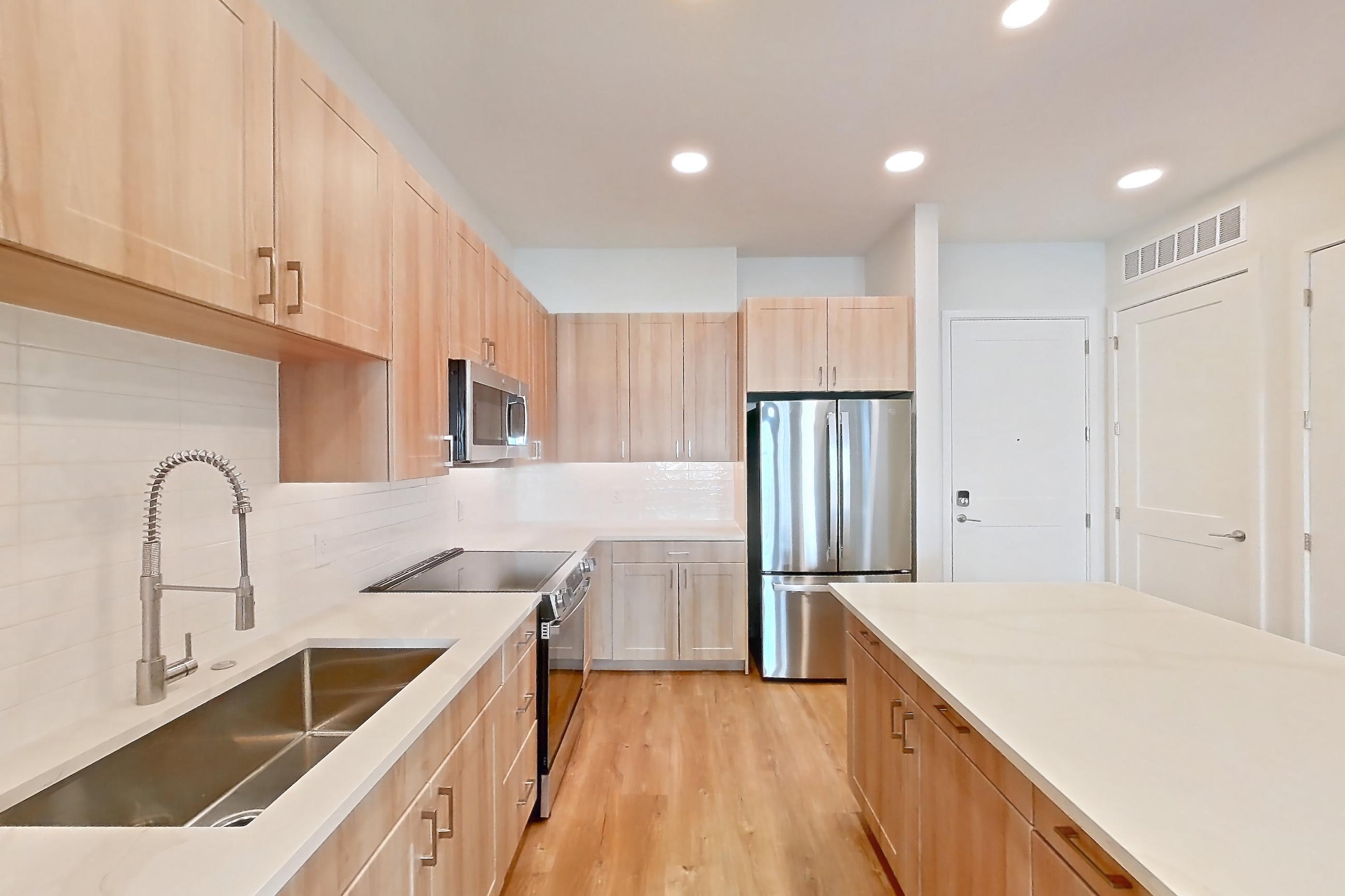 Kitchen with dishwasher, electric range, light countertops, light stone countertops, light wood-finish flooring, microwave, oven/range, refrigerator, and stainless steel appliances, Apartment 252 at Lantower Bayside