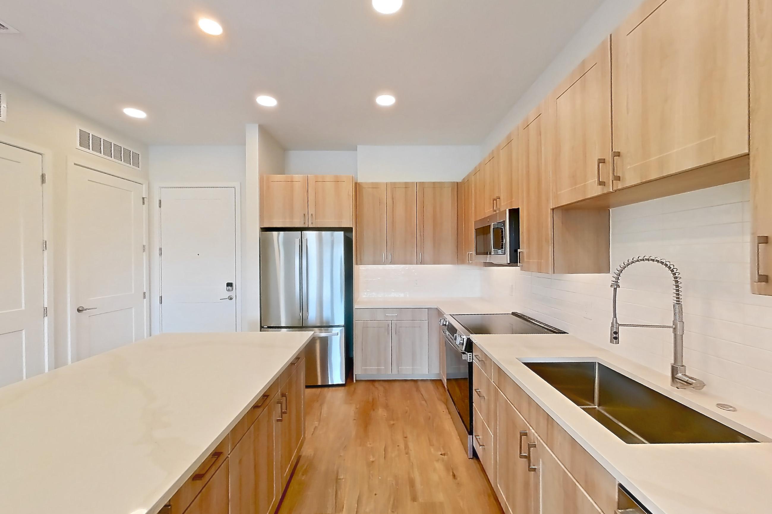 Kitchen with dishwasher, electric range, light countertops, light stone countertops, light wood-finish flooring, microwave, oven/range, refrigerator, and stainless steel appliances, Apartment 253 at Lantower Bayside