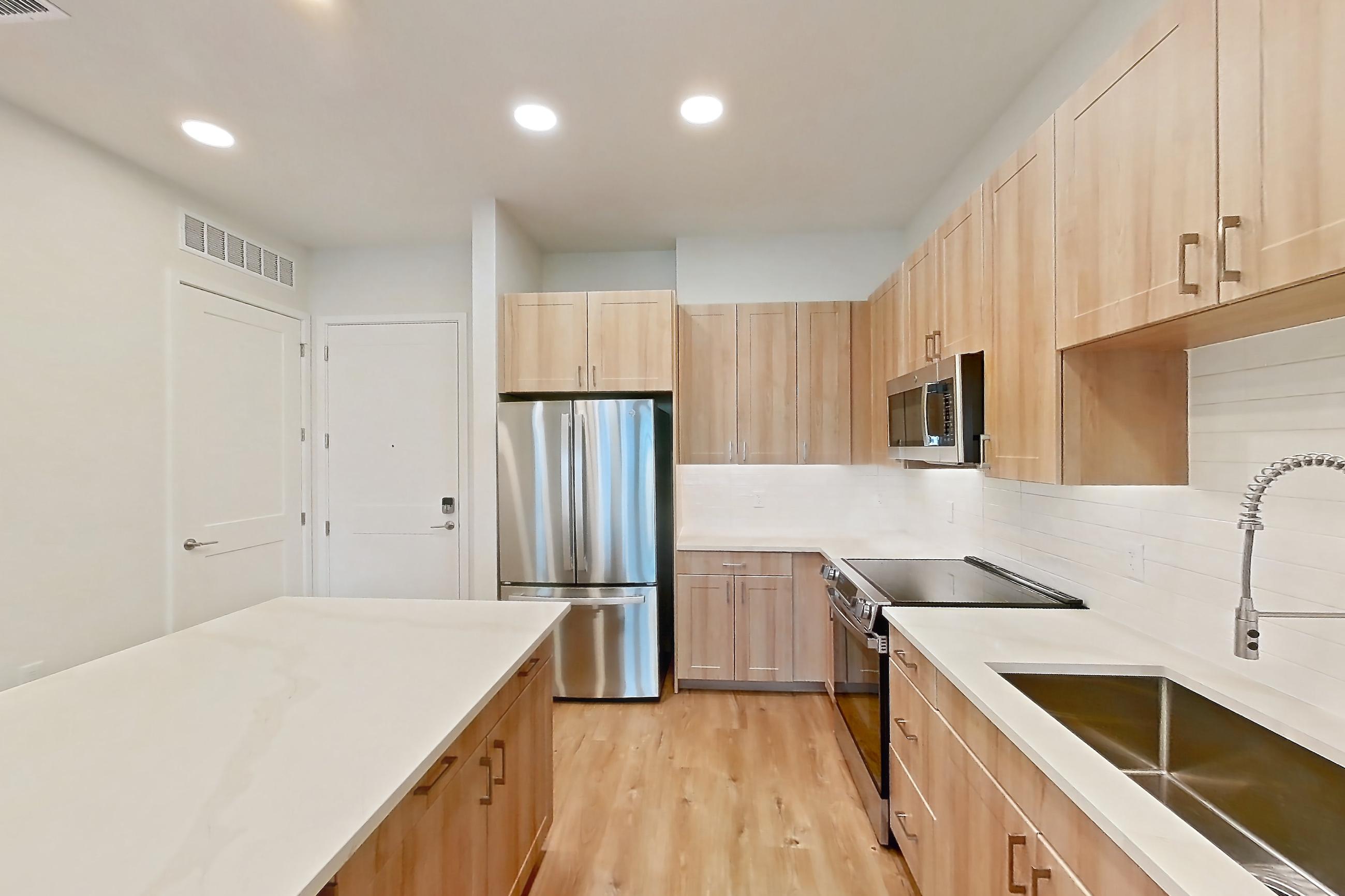Kitchen with dishwasher, electric range, light countertops, light stone countertops, light wood-finish flooring, microwave, oven/range, refrigerator, and stainless steel appliances, Apartment 258 at Lantower Bayside