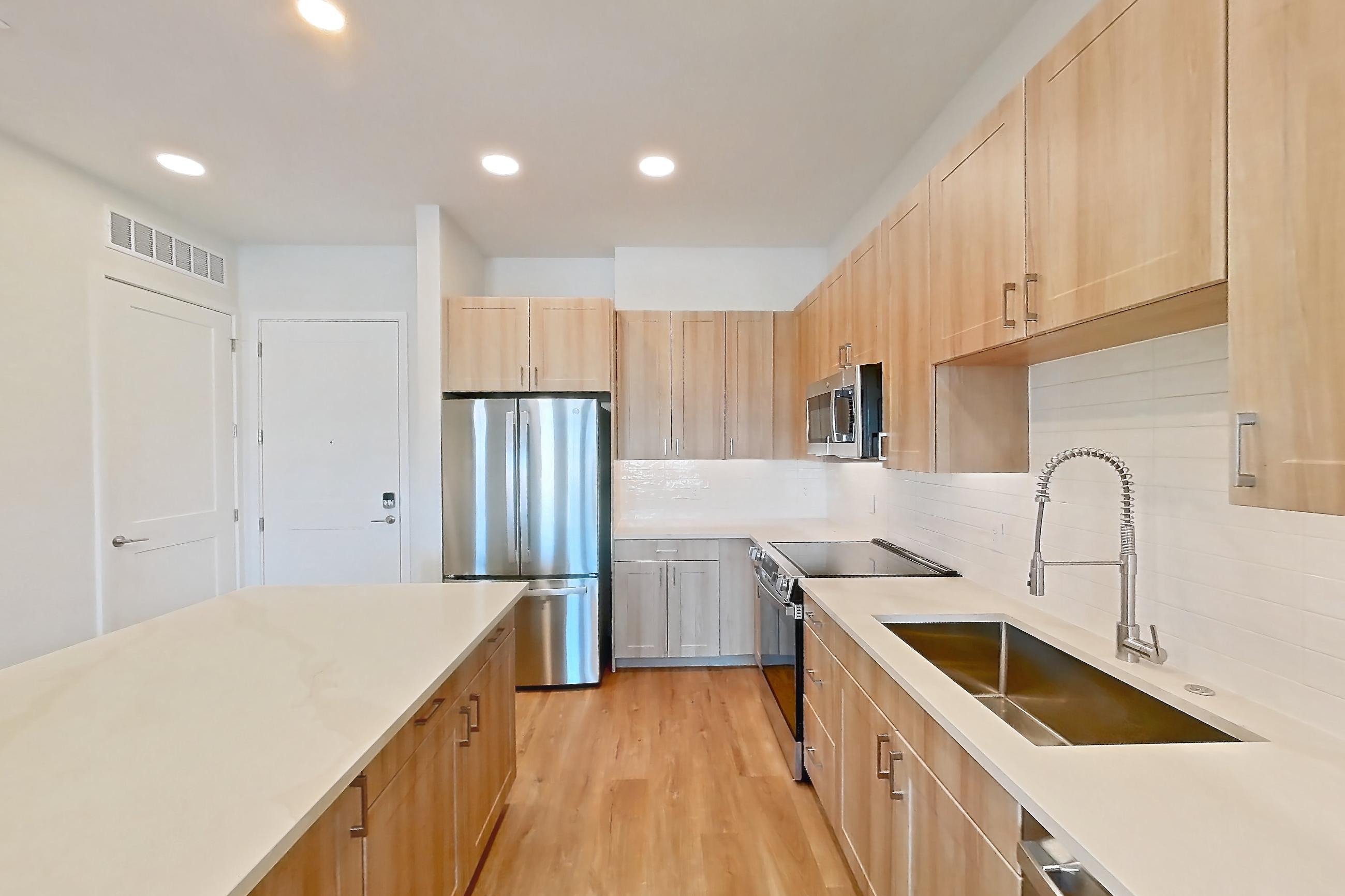 Kitchen with dishwasher, electric range, light countertops, light stone countertops, light wood-finish flooring, microwave, oven/range, refrigerator, and stainless steel appliances, Apartment 259 at Lantower Bayside