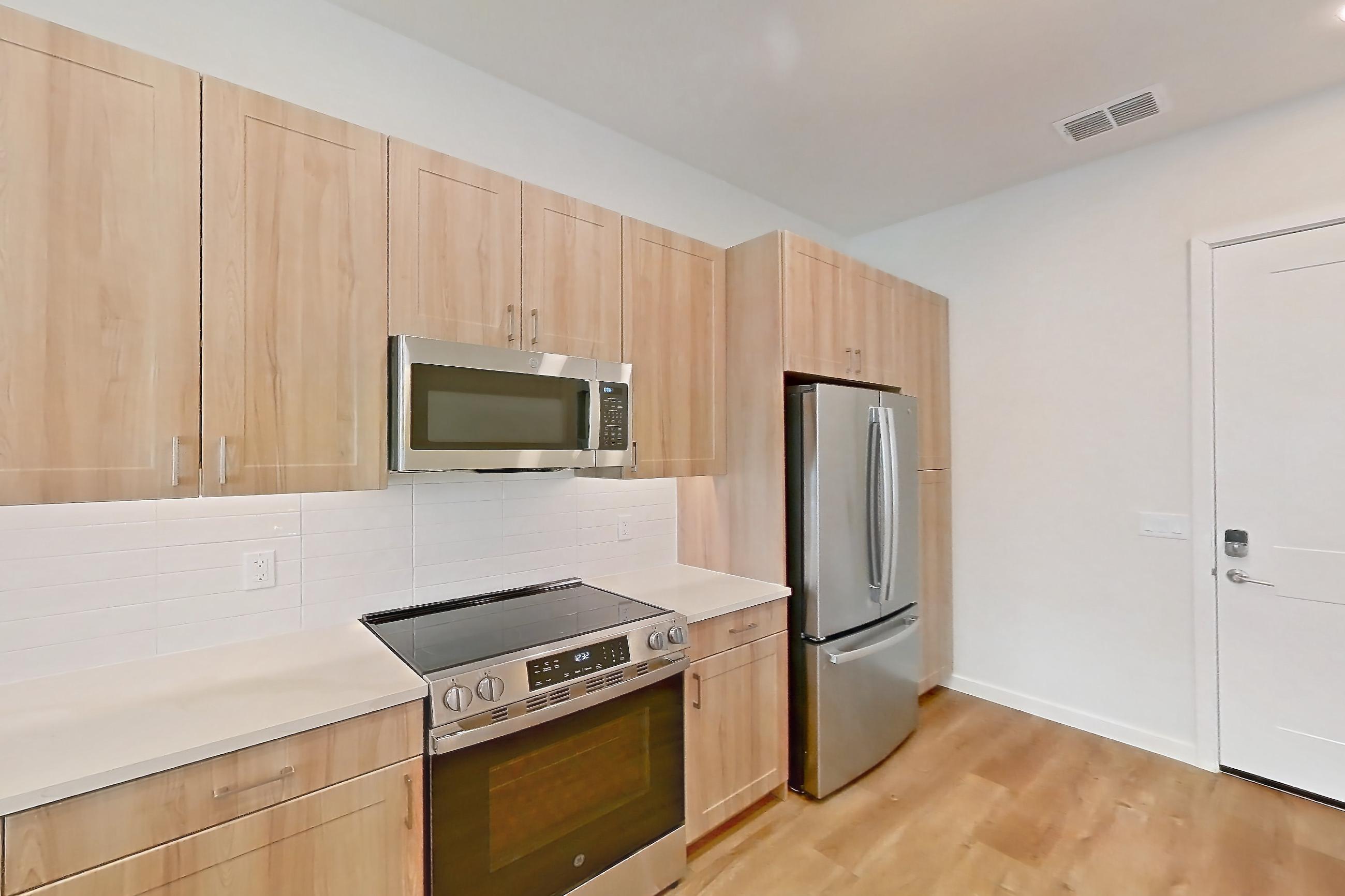 Kitchen with electric range, light countertops, light wood-finish flooring, microwave, oven/range, refrigerator, and stainless steel appliances, Apartment 260 at Lantower Bayside