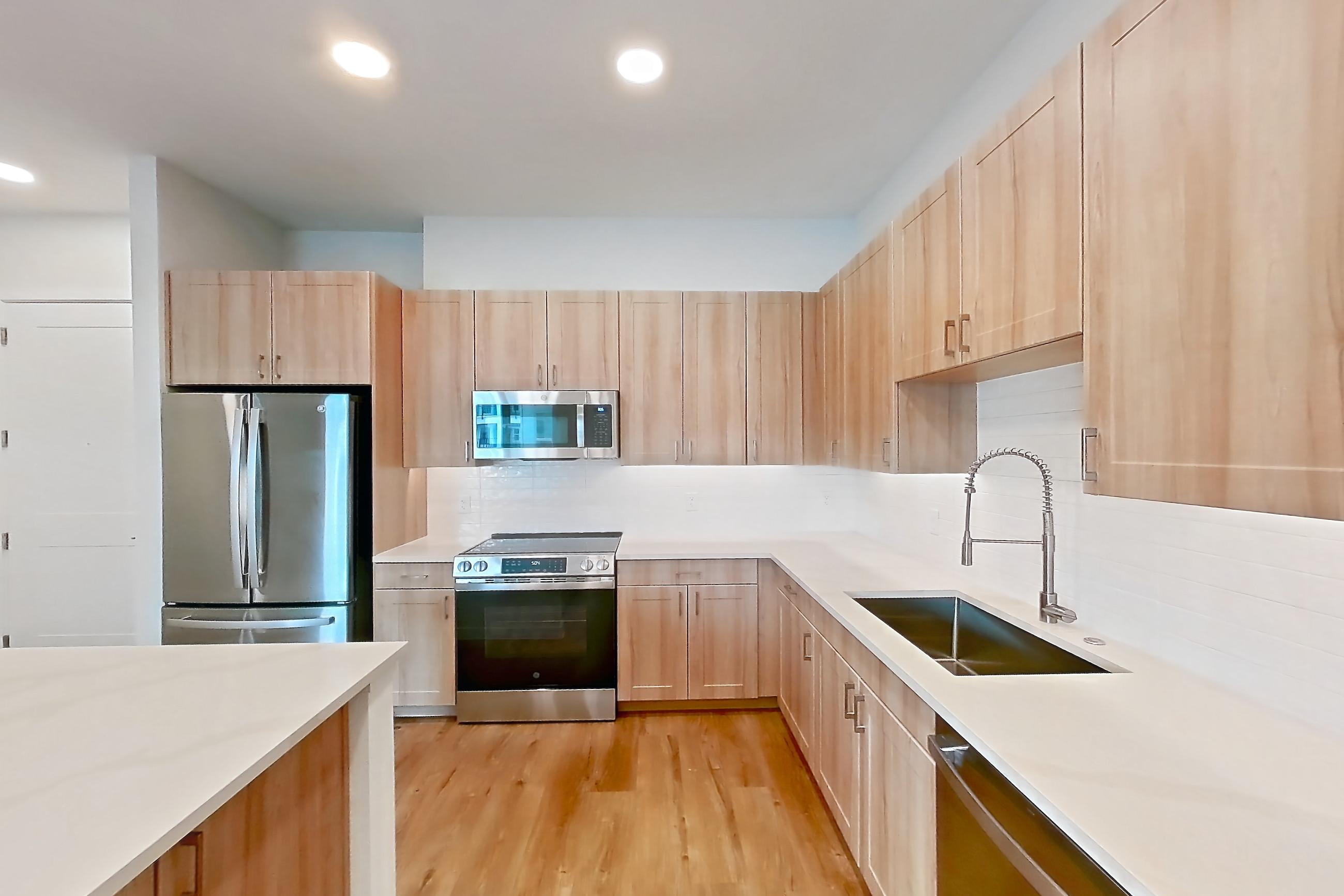 Kitchen with dishwasher, electric range, light countertops, light stone countertops, light wood-finish flooring, microwave, oven/range, refrigerator, and stainless steel appliances, Apartment 332 at Lantower Bayside