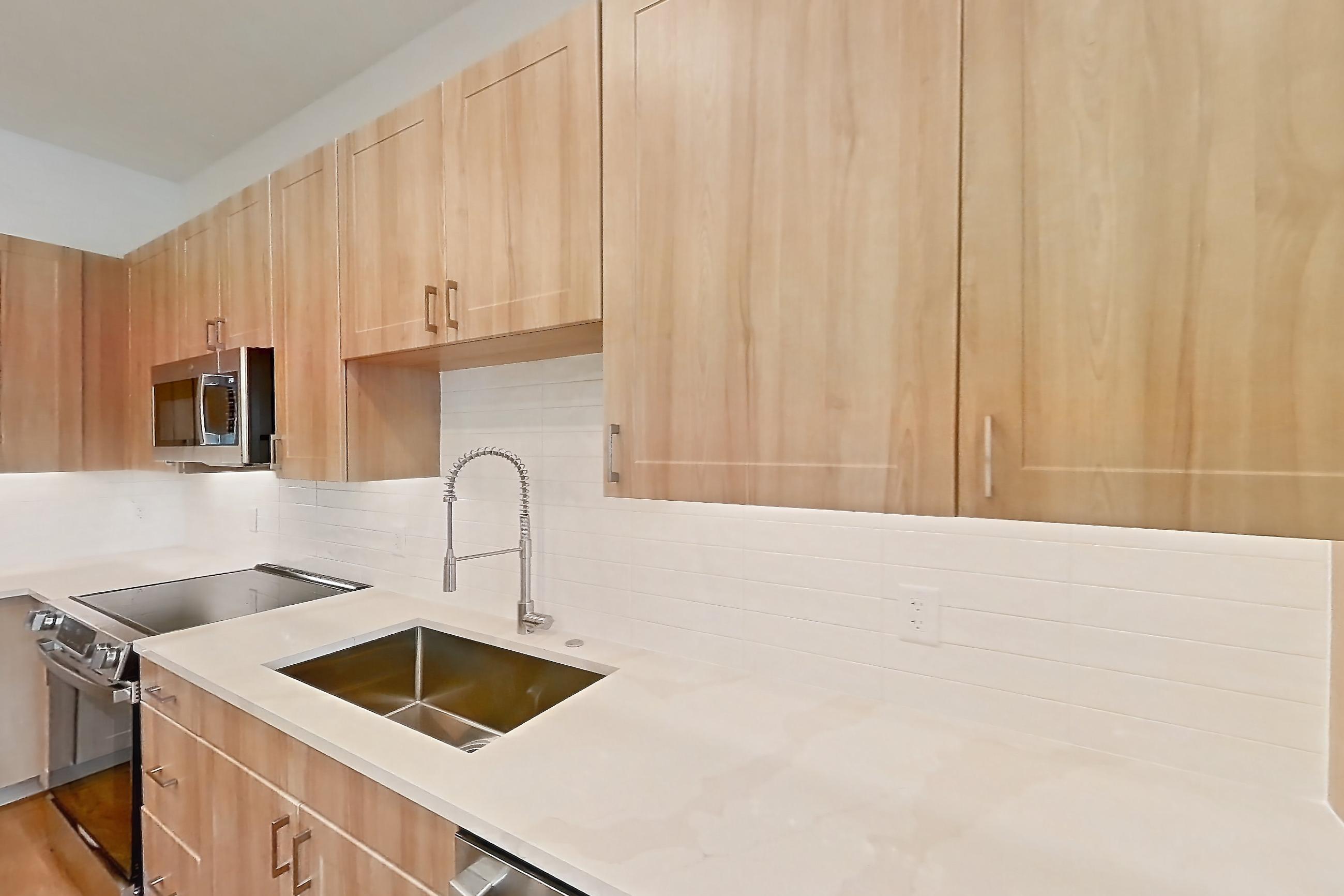 Kitchen with dishwasher, electric range, light countertops, light stone countertops, light wood-finish flooring, microwave, oven/range, refrigerator, and stainless steel appliances, Apartment 333 at Lantower Bayside