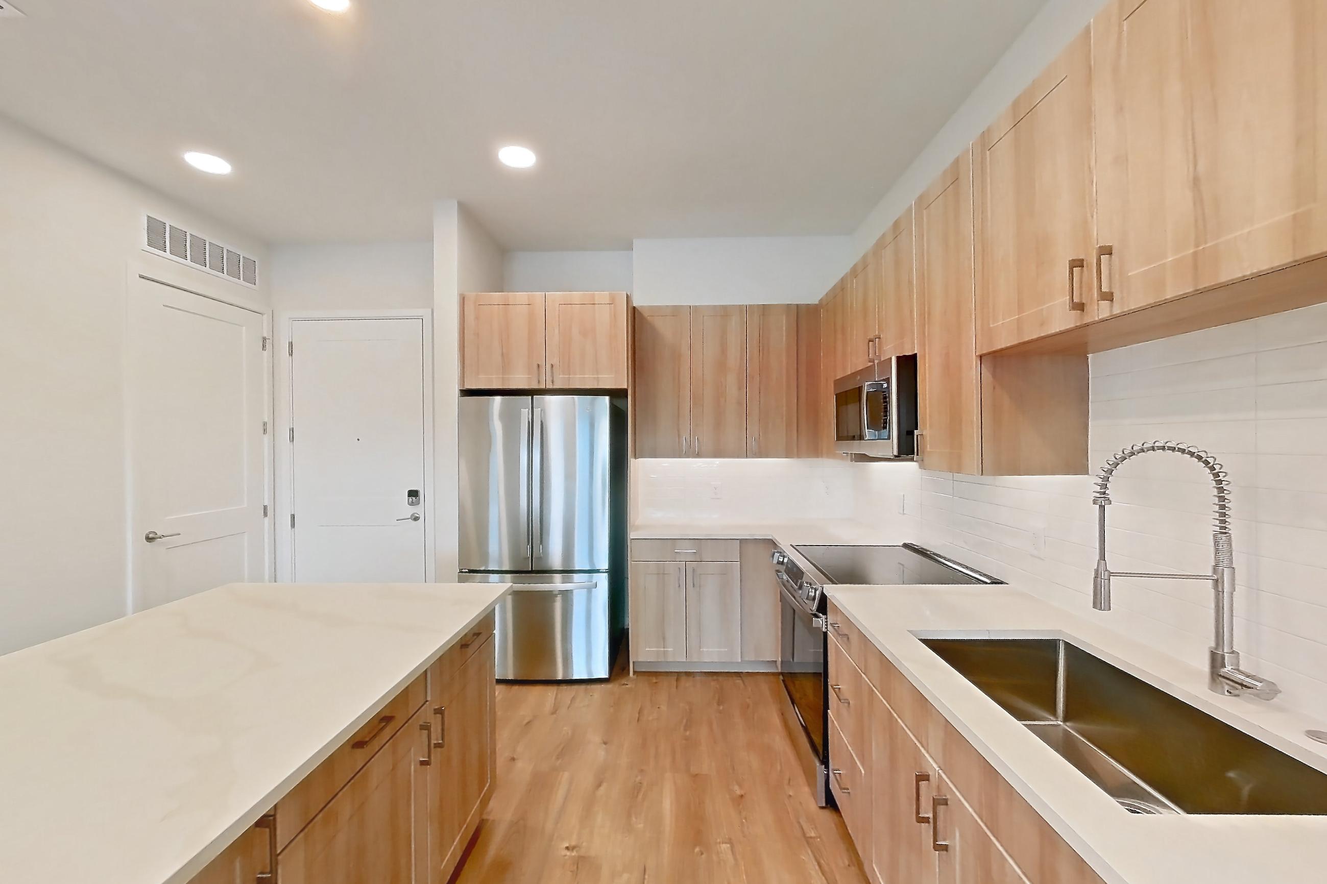 Kitchen with dishwasher, electric range, light countertops, light stone countertops, light wood-finish flooring, microwave, oven/range, refrigerator, and stainless steel appliances, Apartment 333 at Lantower Bayside