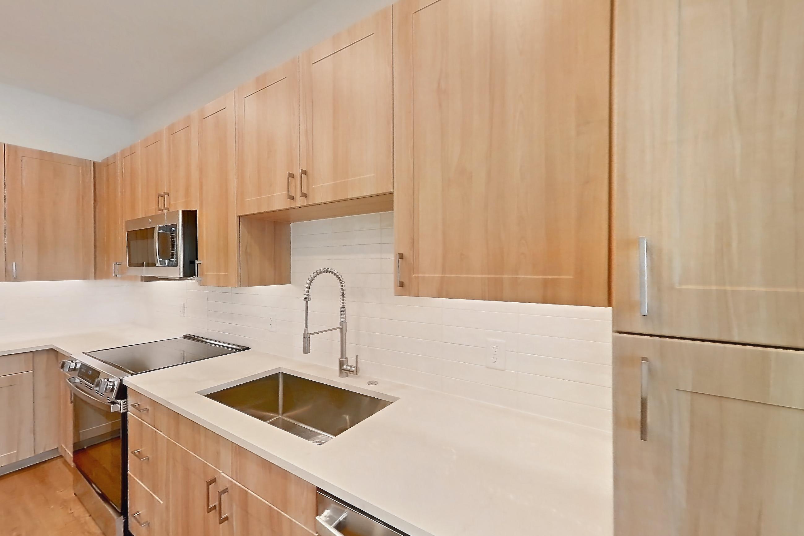 Kitchen with dishwasher, electric range, light countertops, light stone countertops, light wood-finish flooring, oven/range, refrigerator, and stainless steel appliances, Apartment 335 at Lantower Bayside