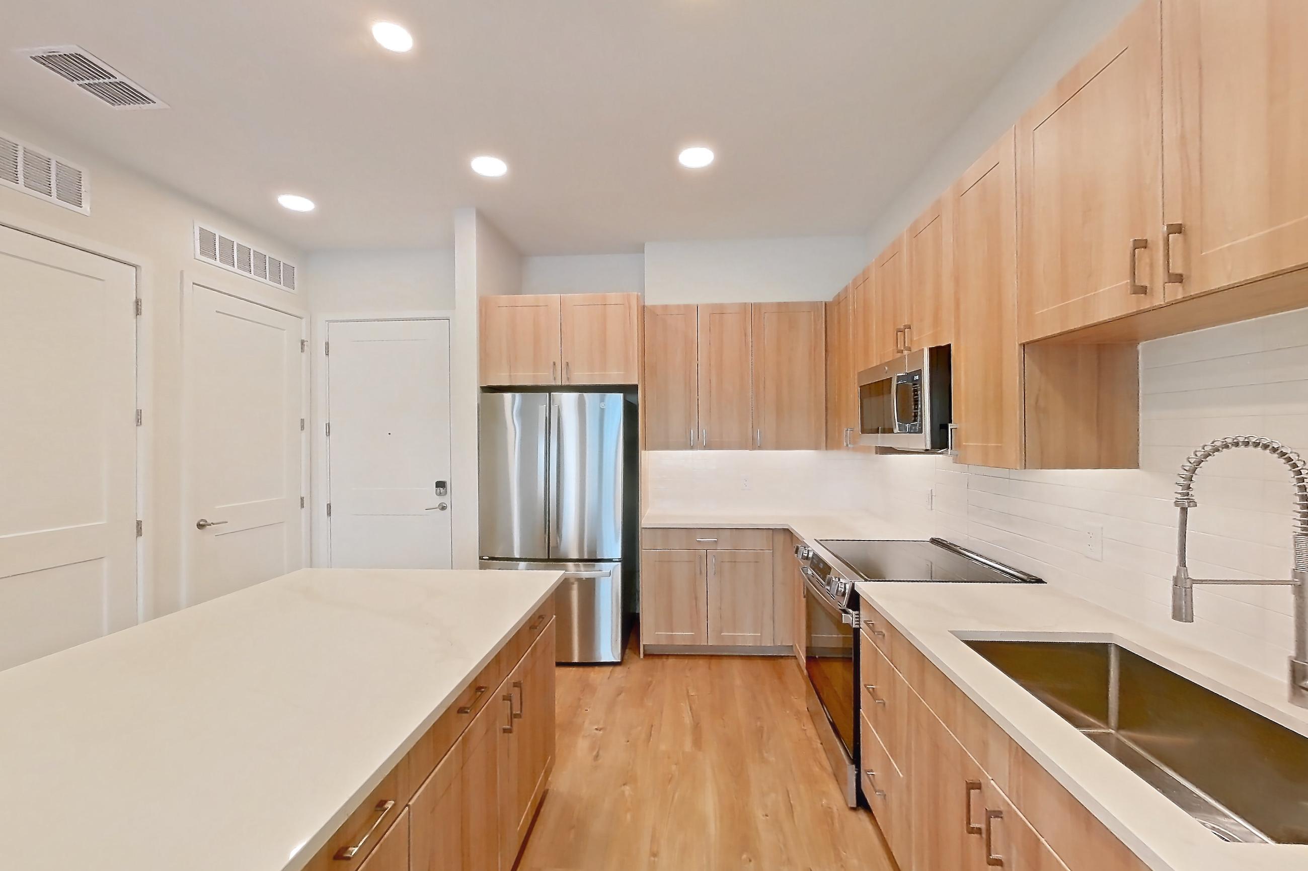 Kitchen with dishwasher, electric range, light countertops, light stone countertops, light wood-finish flooring, oven/range, refrigerator, and stainless steel appliances, Apartment 335 at Lantower Bayside