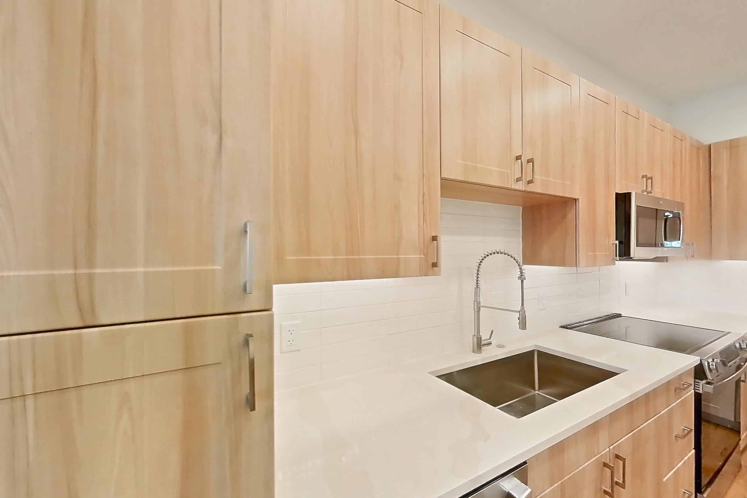 Kitchen with dishwasher, electric range, light countertops, light stone countertops, light wood-finish flooring, microwave, oven/range, refrigerator, and stainless steel appliances, Apartment 336 at Lantower Bayside