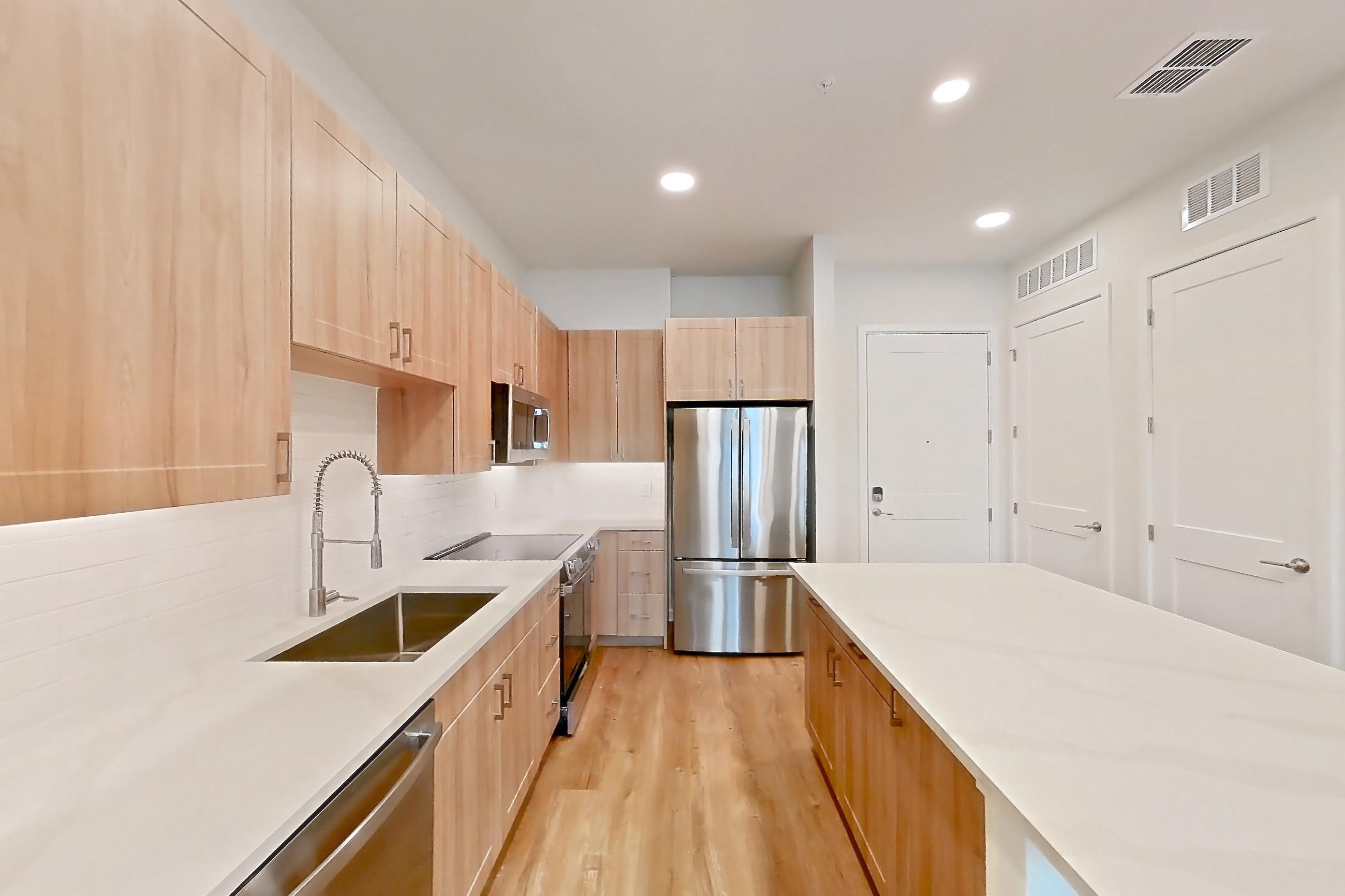 Kitchen with dishwasher, electric range, light stone countertops, light wood-finish flooring, microwave, oven/range, refrigerator, and stainless steel appliances, Apartment 338 at Lantower Bayside
