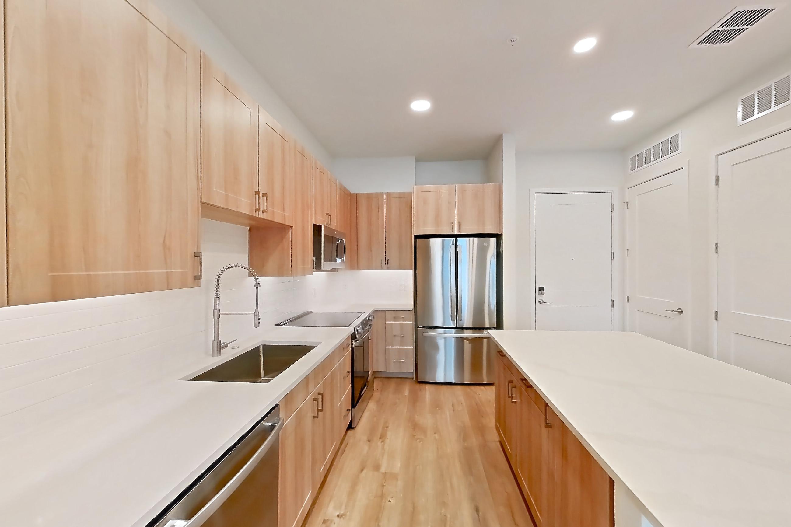 Kitchen with dishwasher, electric range, light countertops, light stone countertops, light wood-finish flooring, microwave, oven/range, refrigerator, and stainless steel appliances, Apartment 339 at Lantower Bayside