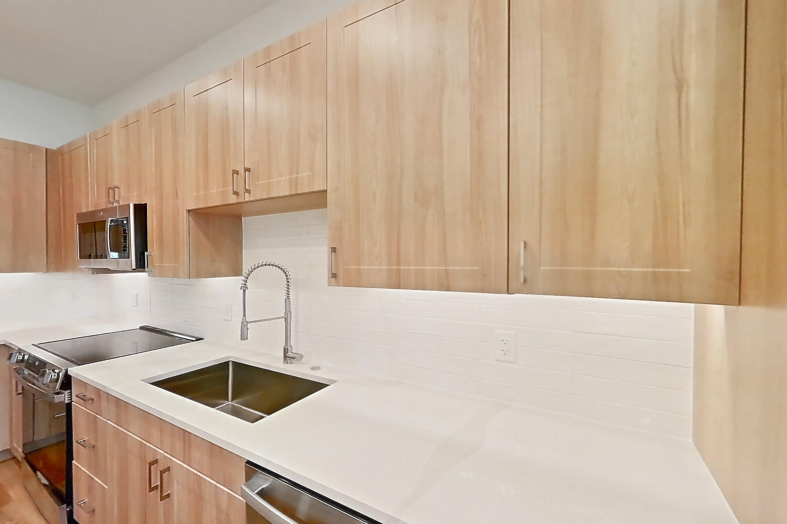 Kitchen with dishwasher, electric range, light countertops, light stone countertops, light wood-finish flooring, microwave, oven/range, refrigerator, and stainless steel appliances, Apartment 340 at Lantower Bayside
