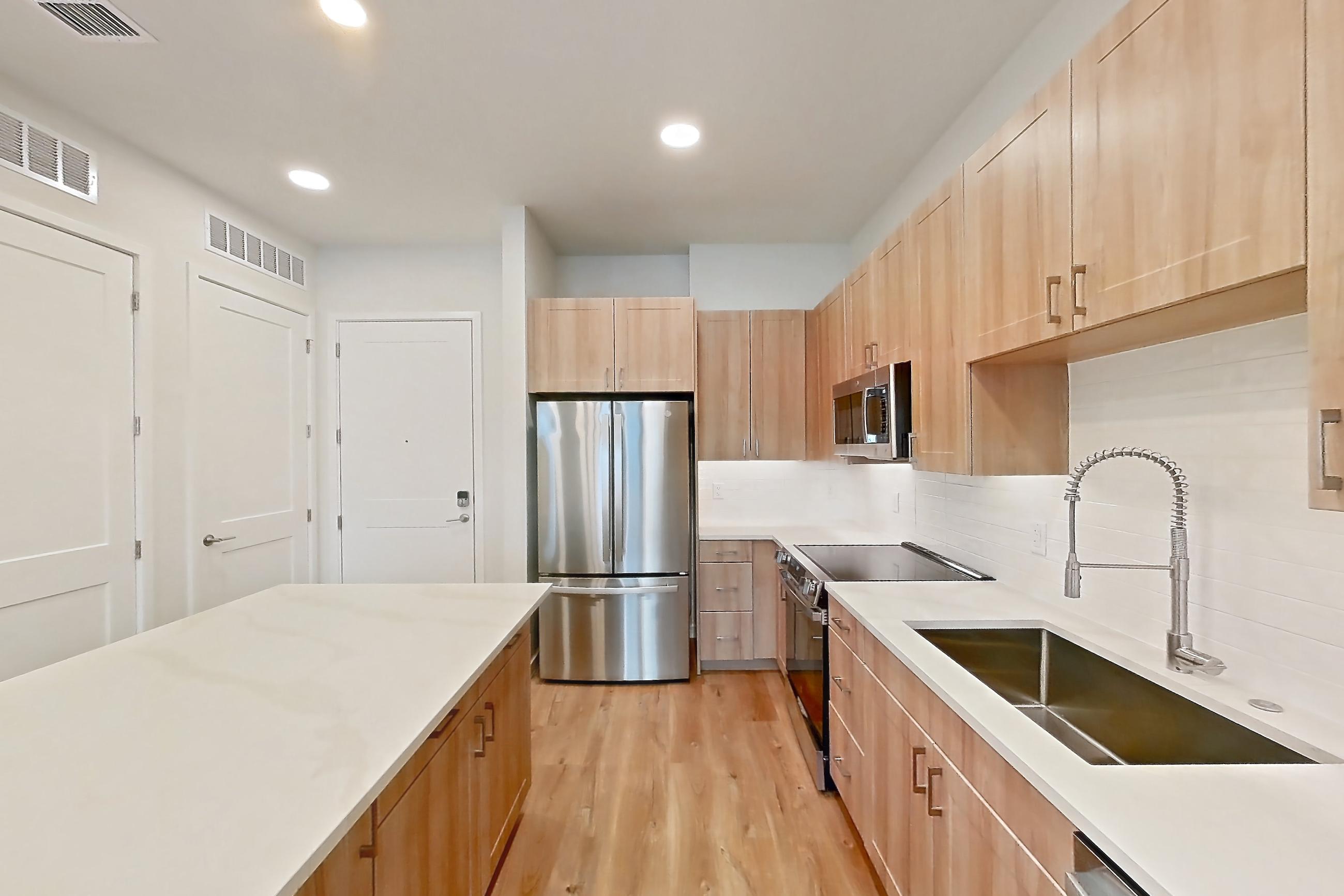 Kitchen with dishwasher, electric range, light countertops, light stone countertops, light wood-finish flooring, microwave, oven/range, refrigerator, and stainless steel appliances, Apartment 340 at Lantower Bayside