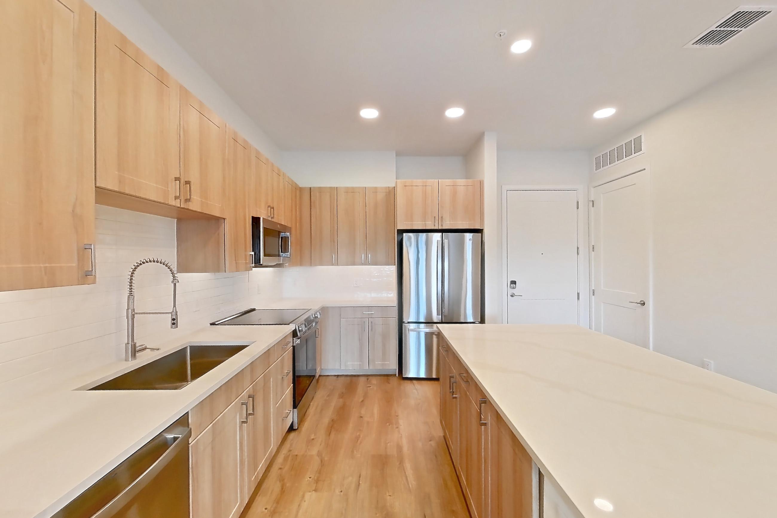 Kitchen with dishwasher, electric range, light countertops, light stone countertops, light wood-finish flooring, oven/range, refrigerator, and stainless steel appliances, Apartment 431 at Lantower Bayside