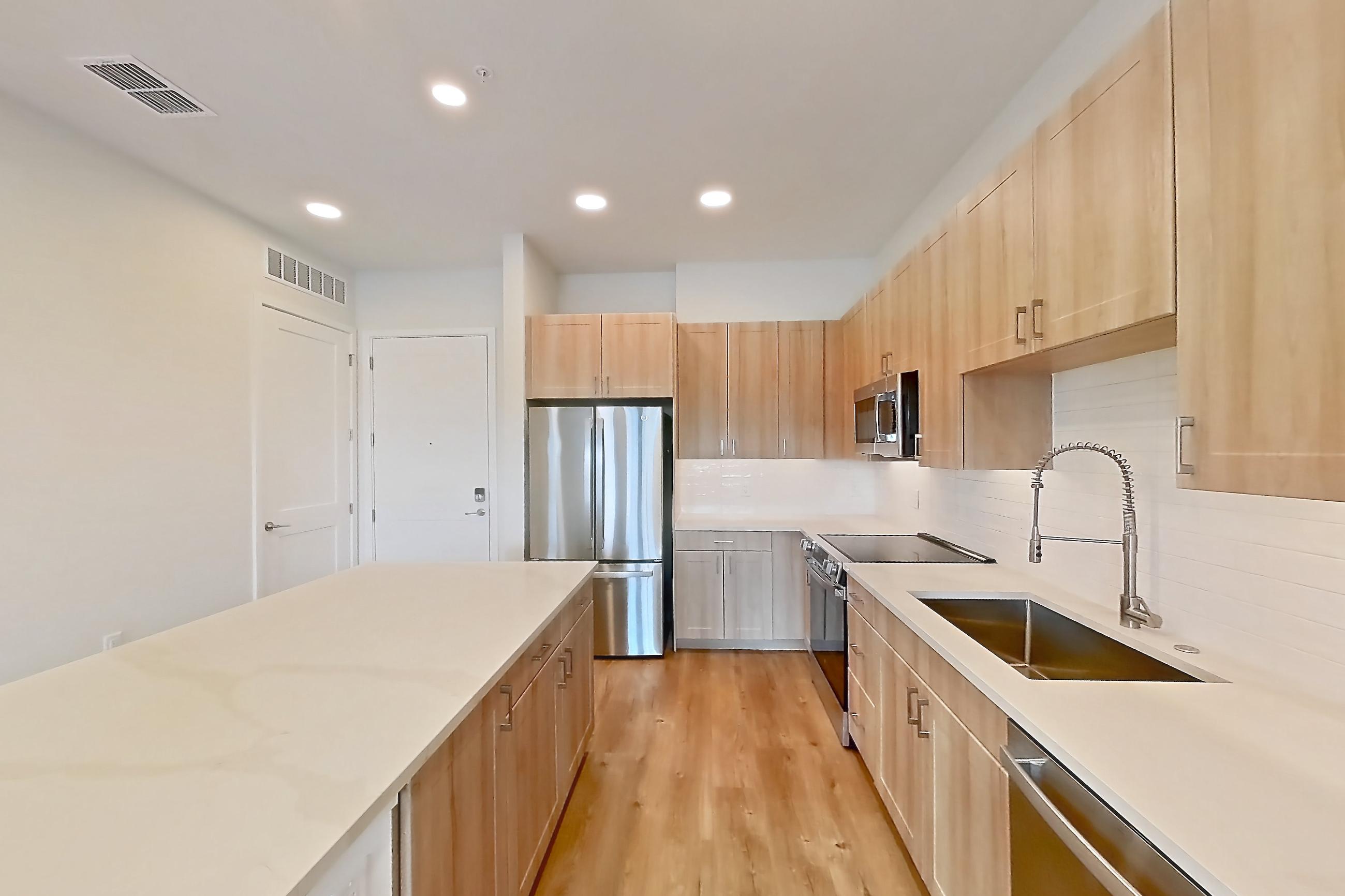 Kitchen with dishwasher, electric range, light countertops, light stone countertops, light wood-finish flooring, microwave, oven/range, refrigerator, and stainless steel appliances, Apartment 433 at Lantower Bayside