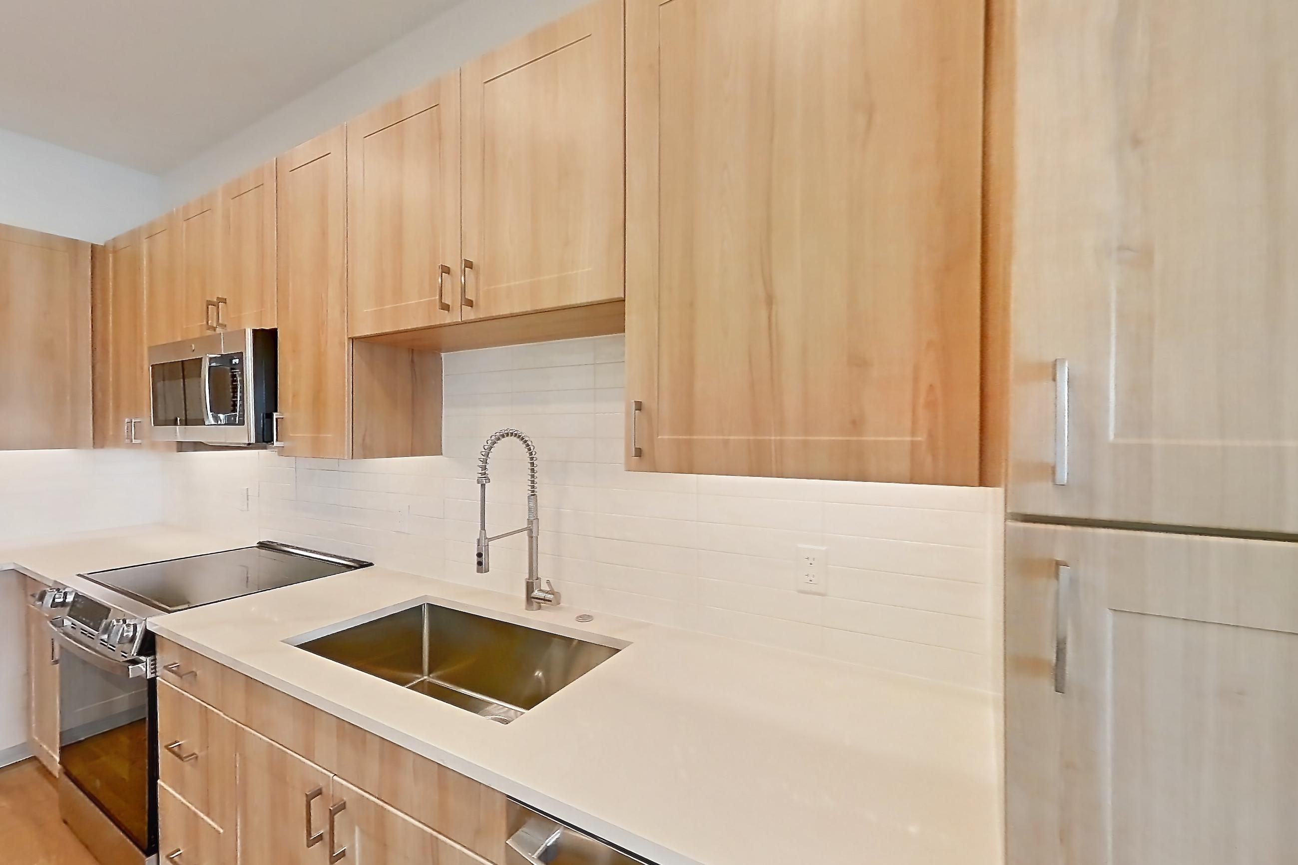 Kitchen with dishwasher, electric range, light countertops, light stone countertops, light wood-finish flooring, microwave, oven/range, refrigerator, and stainless steel appliances, Apartment 435 at Lantower Bayside