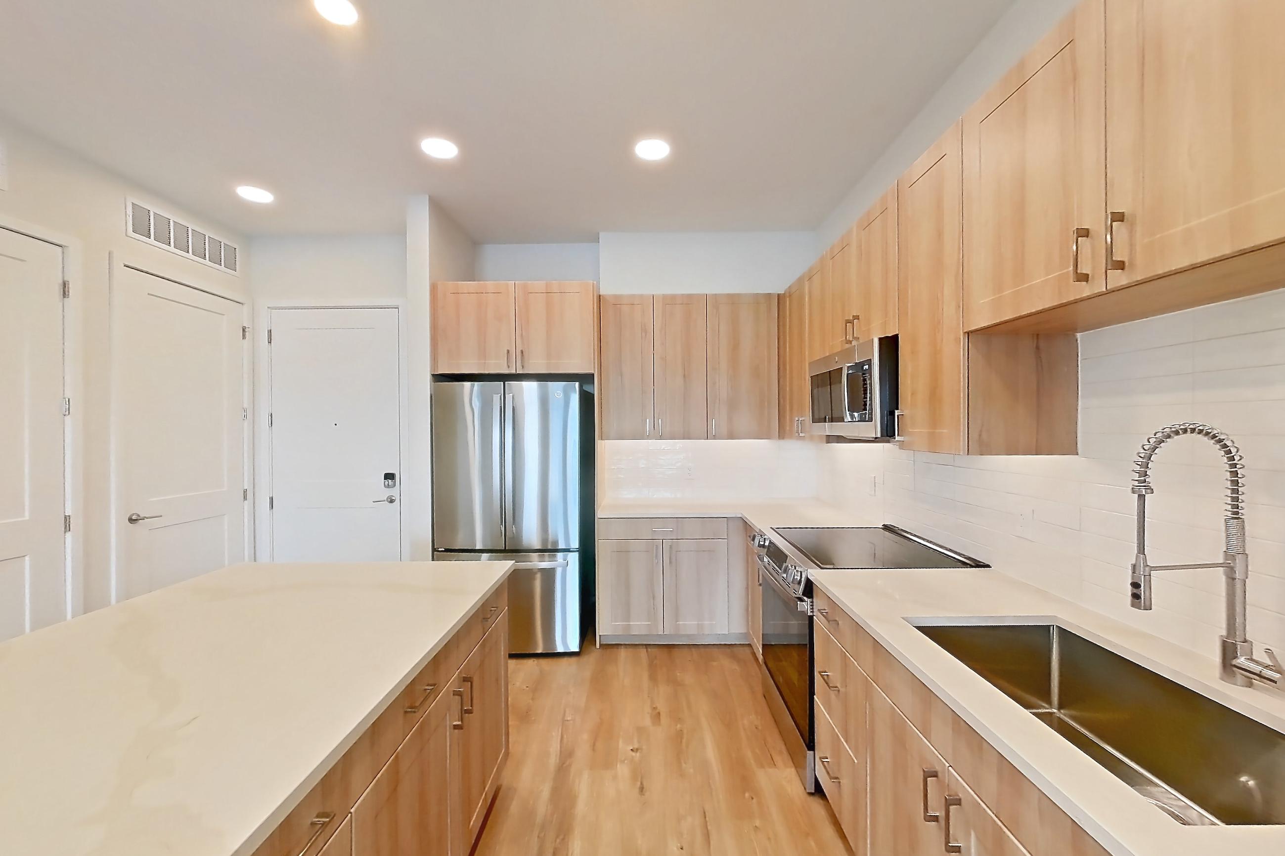 Kitchen with dishwasher, electric range, light countertops, light stone countertops, light wood-finish flooring, microwave, oven/range, refrigerator, and stainless steel appliances, Apartment 435 at Lantower Bayside