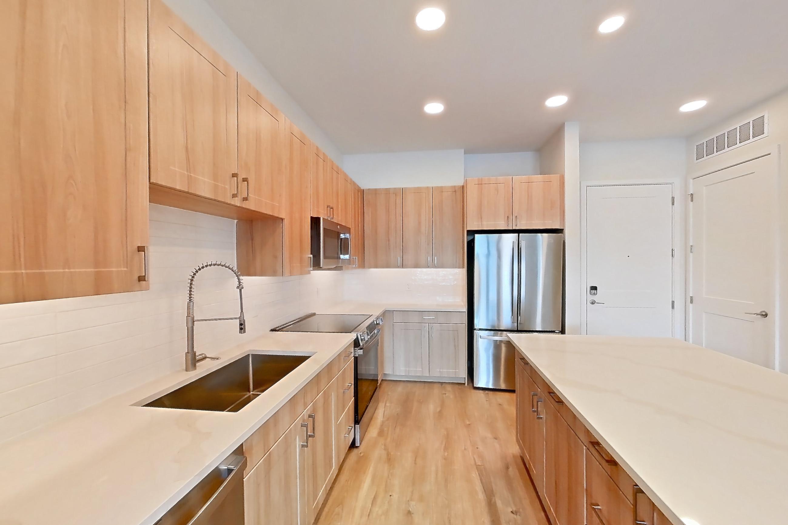 Kitchen with dishwasher, electric range, light countertops, light stone countertops, light wood-finish flooring, microwave, oven/range, refrigerator, and stainless steel appliances, Apartment 436 at Lantower Bayside