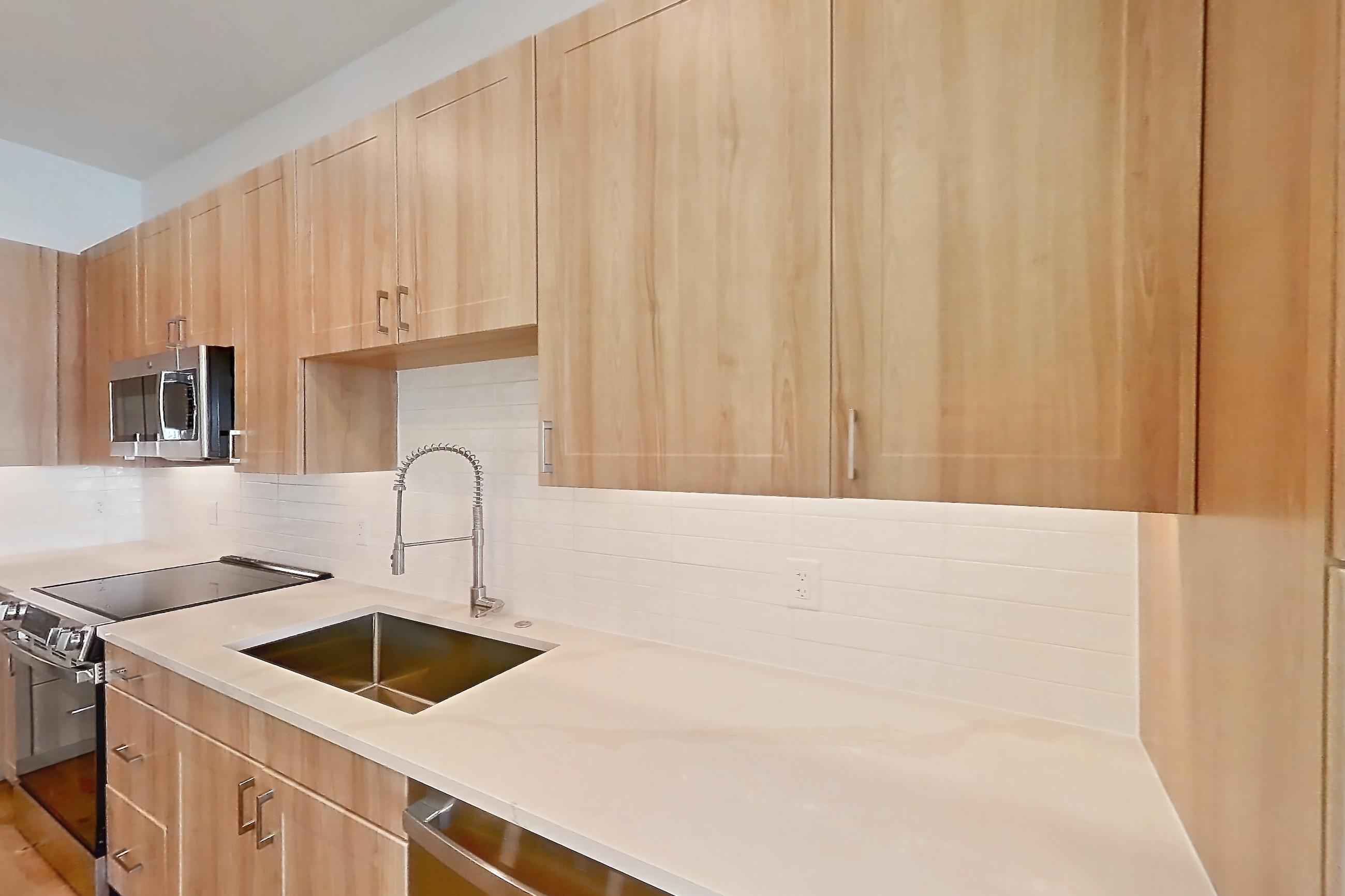 Kitchen with dishwasher, electric range, light countertops, light stone countertops, light wood-finish flooring, microwave, oven/range, refrigerator, and stainless steel appliances, Apartment 437 at Lantower Bayside
