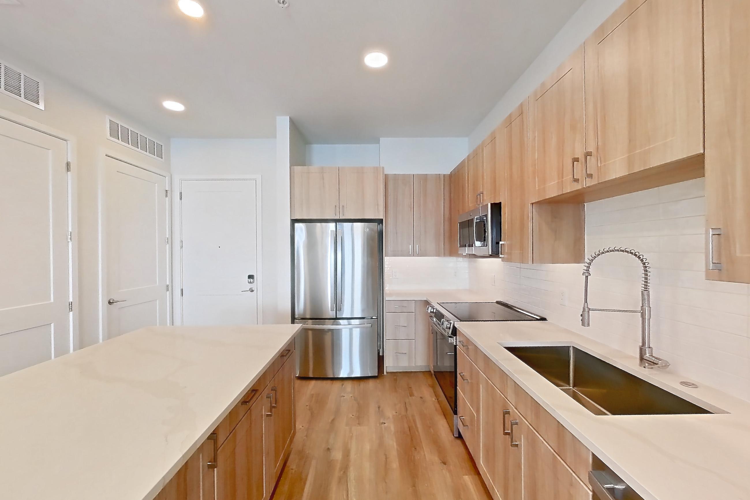 Kitchen with dishwasher, electric range, light countertops, light stone countertops, light wood-finish flooring, microwave, oven/range, refrigerator, and stainless steel appliances, Apartment 437 at Lantower Bayside