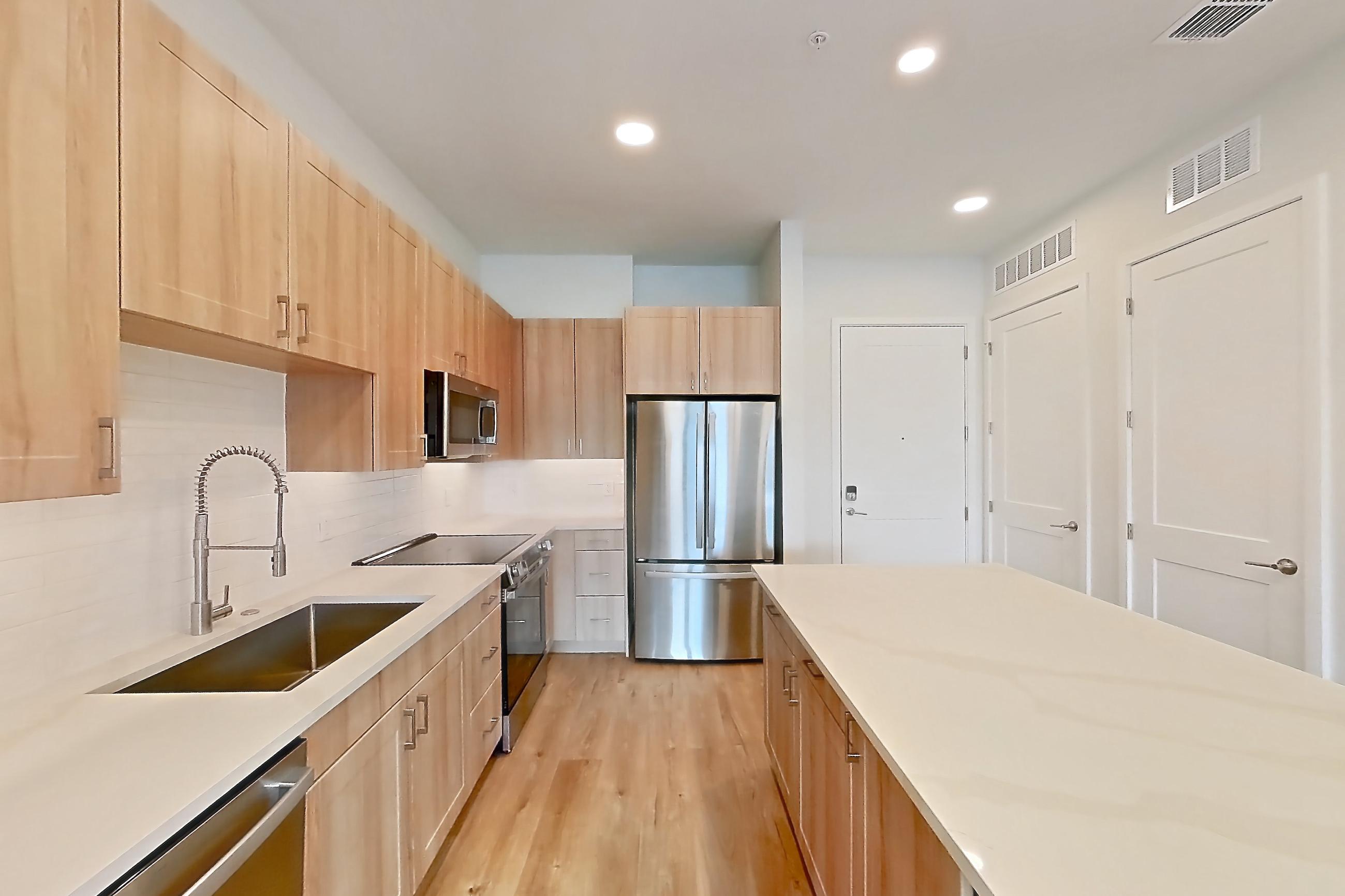 Kitchen with dishwasher, electric range, light stone countertops, light wood-finish flooring, microwave, oven/range, refrigerator, and stainless steel appliances, Apartment 438 at Lantower Bayside