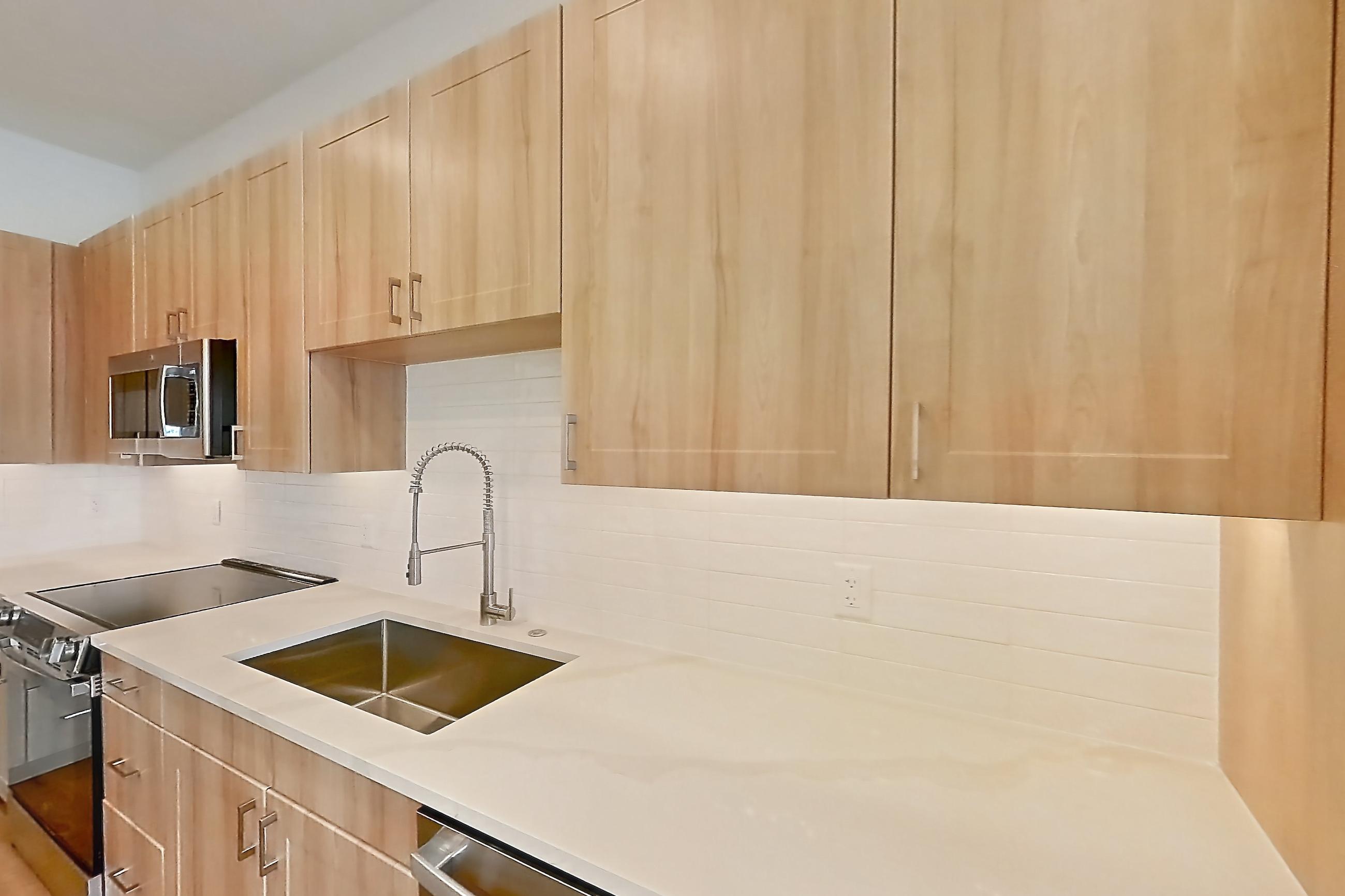 Kitchen with dishwasher, electric range, light countertops, light stone countertops, light wood-finish flooring, microwave, oven/range, refrigerator, and stainless steel appliances, Apartment 440 at Lantower Bayside