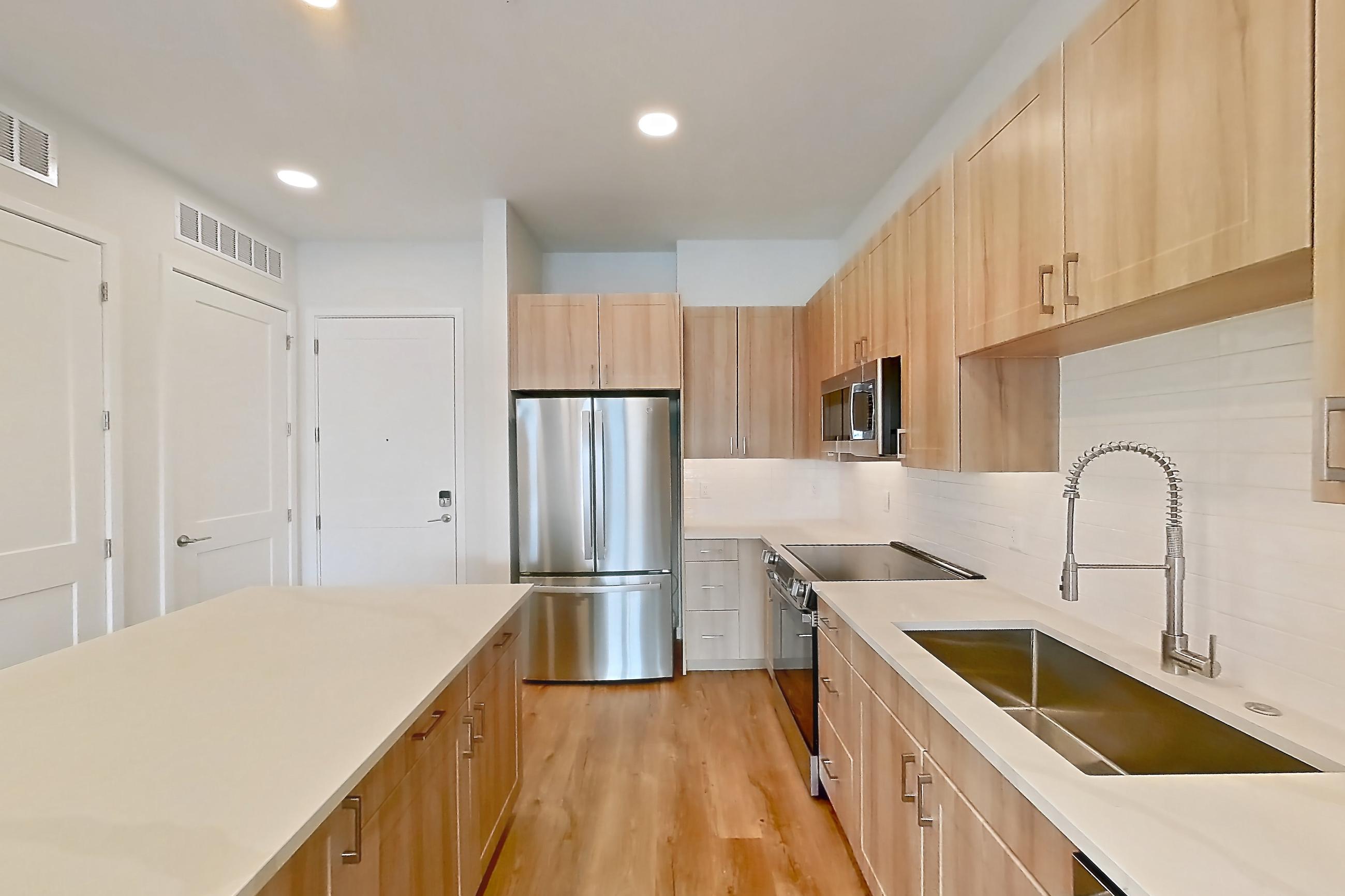 Kitchen with dishwasher, electric range, light countertops, light stone countertops, light wood-finish flooring, microwave, oven/range, refrigerator, and stainless steel appliances, Apartment 440 at Lantower Bayside