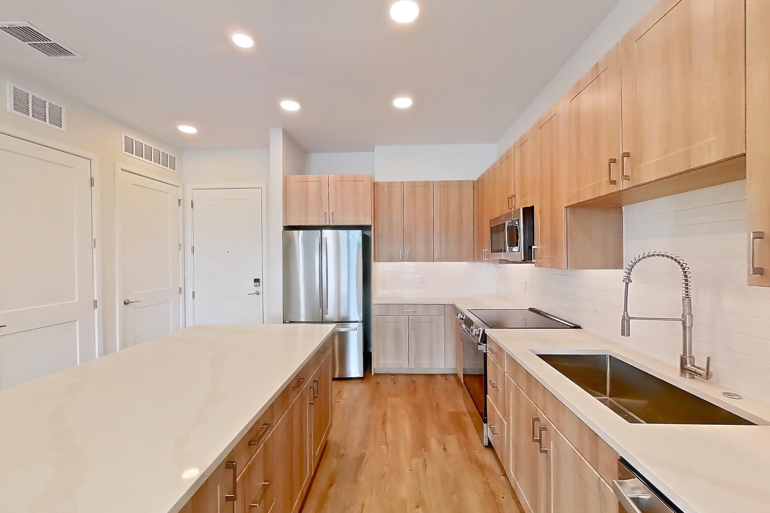 Kitchen with dishwasher, electric range, light countertops, light stone countertops, light wood-finish flooring, oven/range, refrigerator, and stainless steel appliances, Apartment 442 at Lantower Bayside