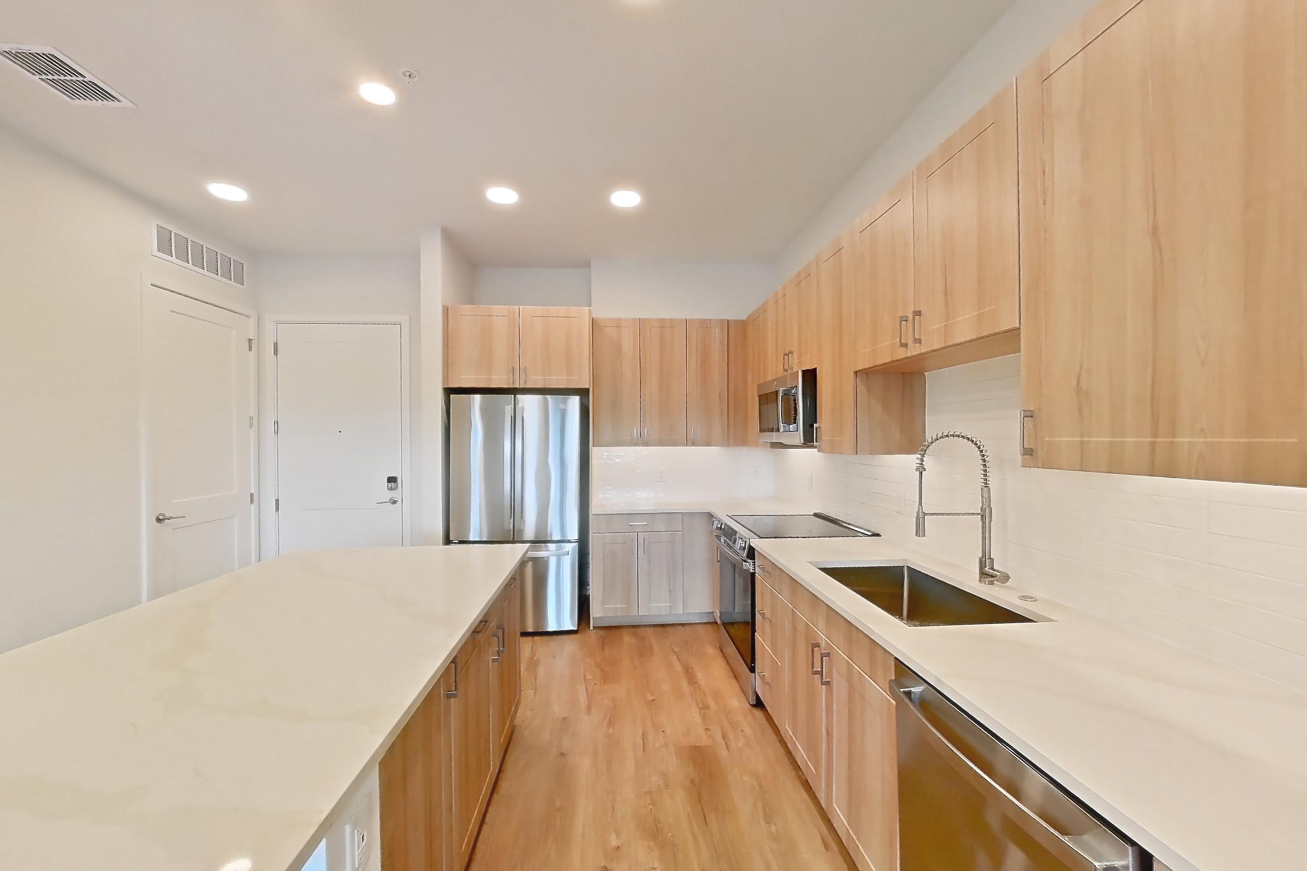 Kitchen with dishwasher, electric range, light countertops, light stone countertops, light wood-finish flooring, microwave, oven/range, refrigerator, and stainless steel appliances, Apartment 445 at Lantower Bayside