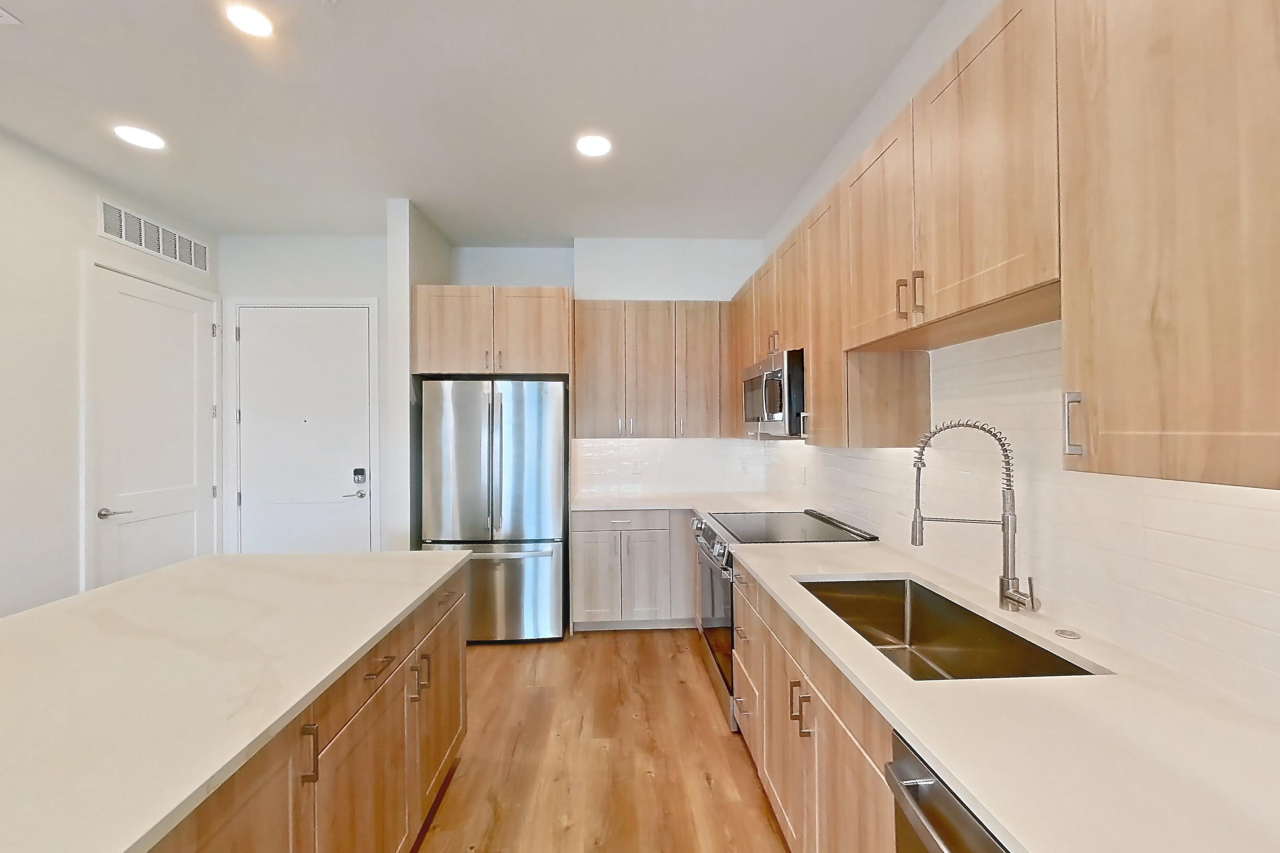 Kitchen with dishwasher, electric range, light countertops, light stone countertops, light wood-finish flooring, microwave, oven/range, refrigerator, and stainless steel appliances, Apartment 446 at Lantower Bayside