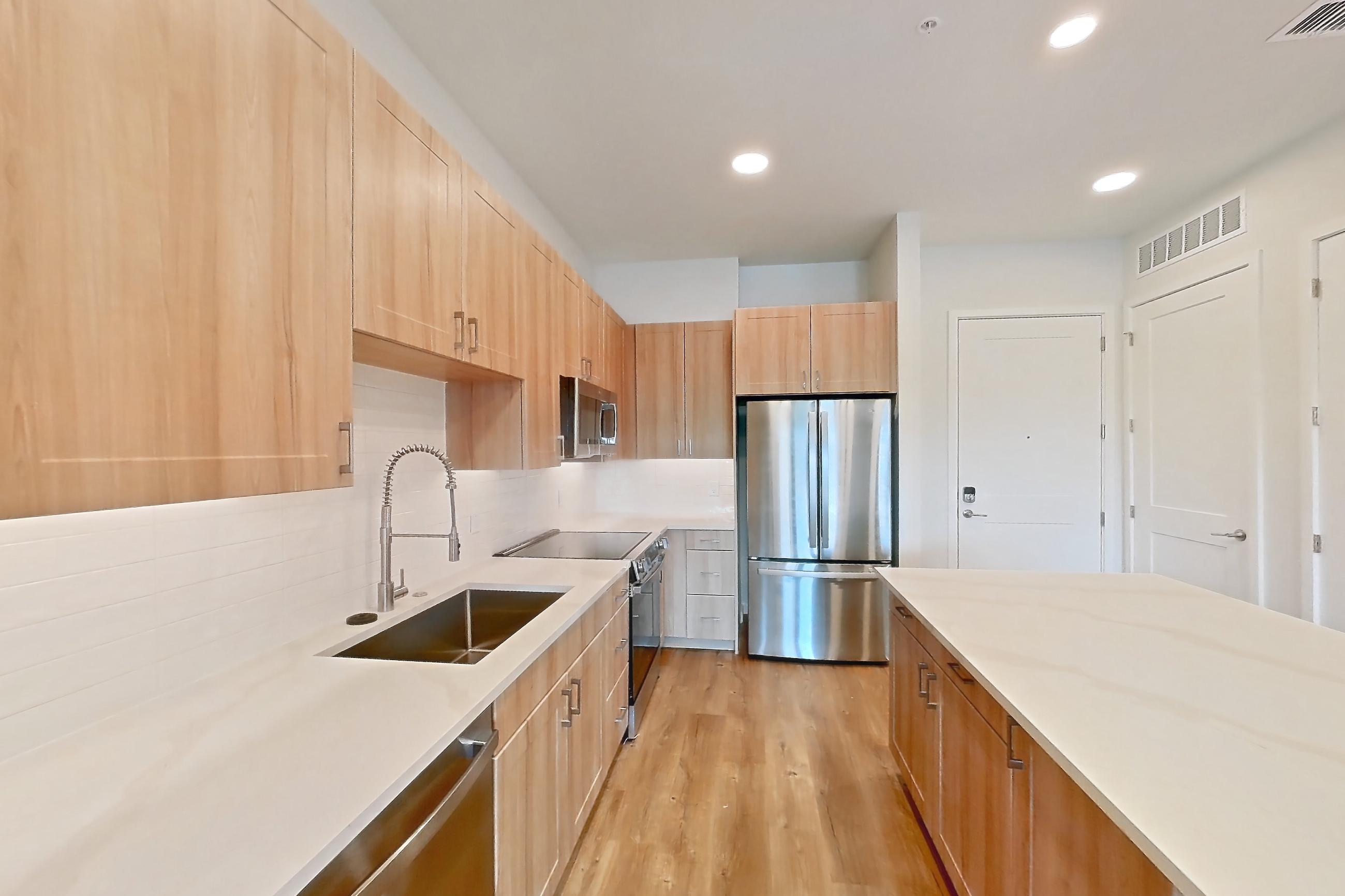 Kitchen with dishwasher, electric range, light countertops, light stone countertops, light wood-finish flooring, microwave, oven/range, refrigerator, and stainless steel appliances, Apartment 447 at Lantower Bayside
