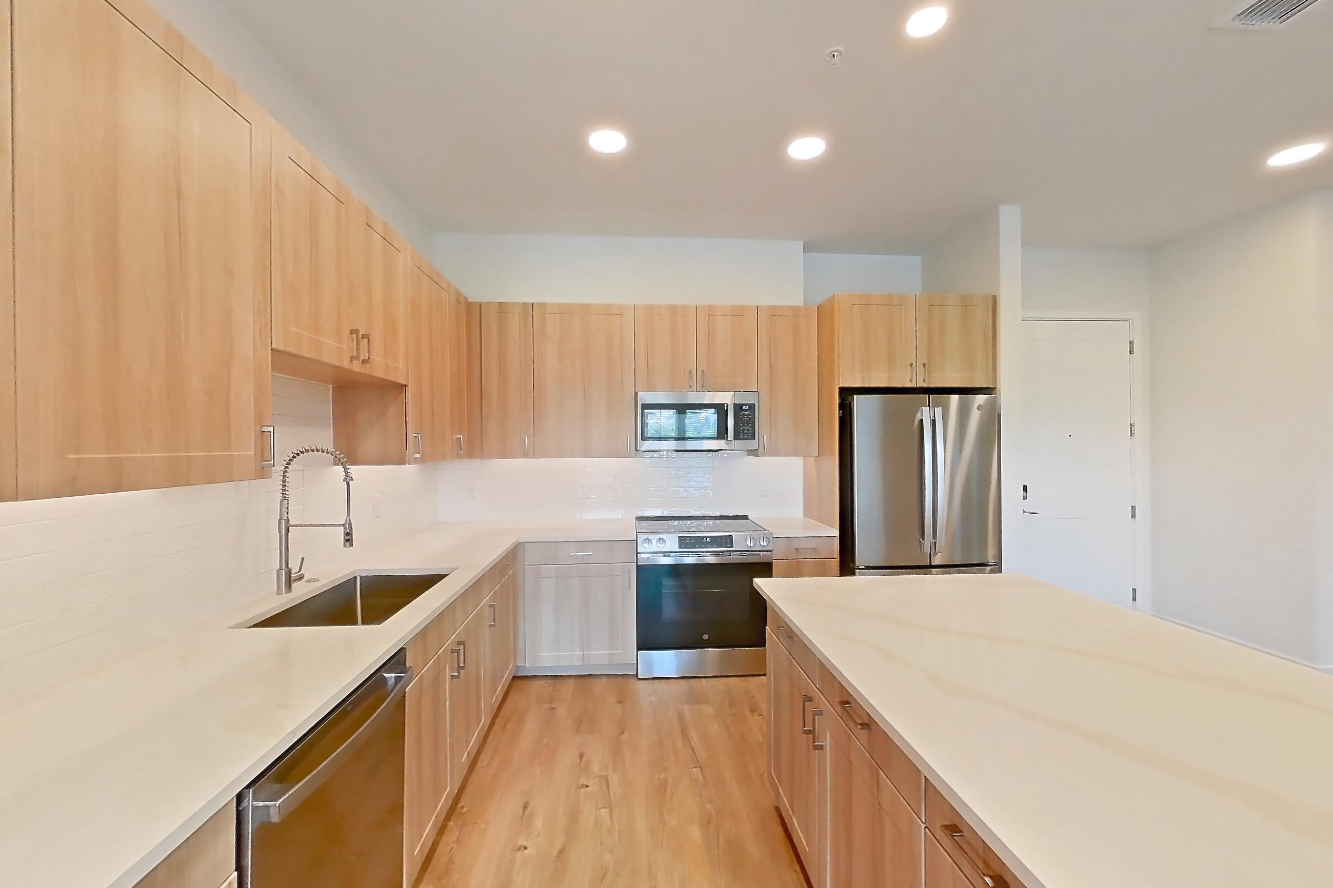 Kitchen with dishwasher, electric range, light countertops, light stone countertops, light wood-finish flooring, microwave, oven/range, refrigerator, and stainless steel appliances, Apartment 449 at Lantower Bayside
