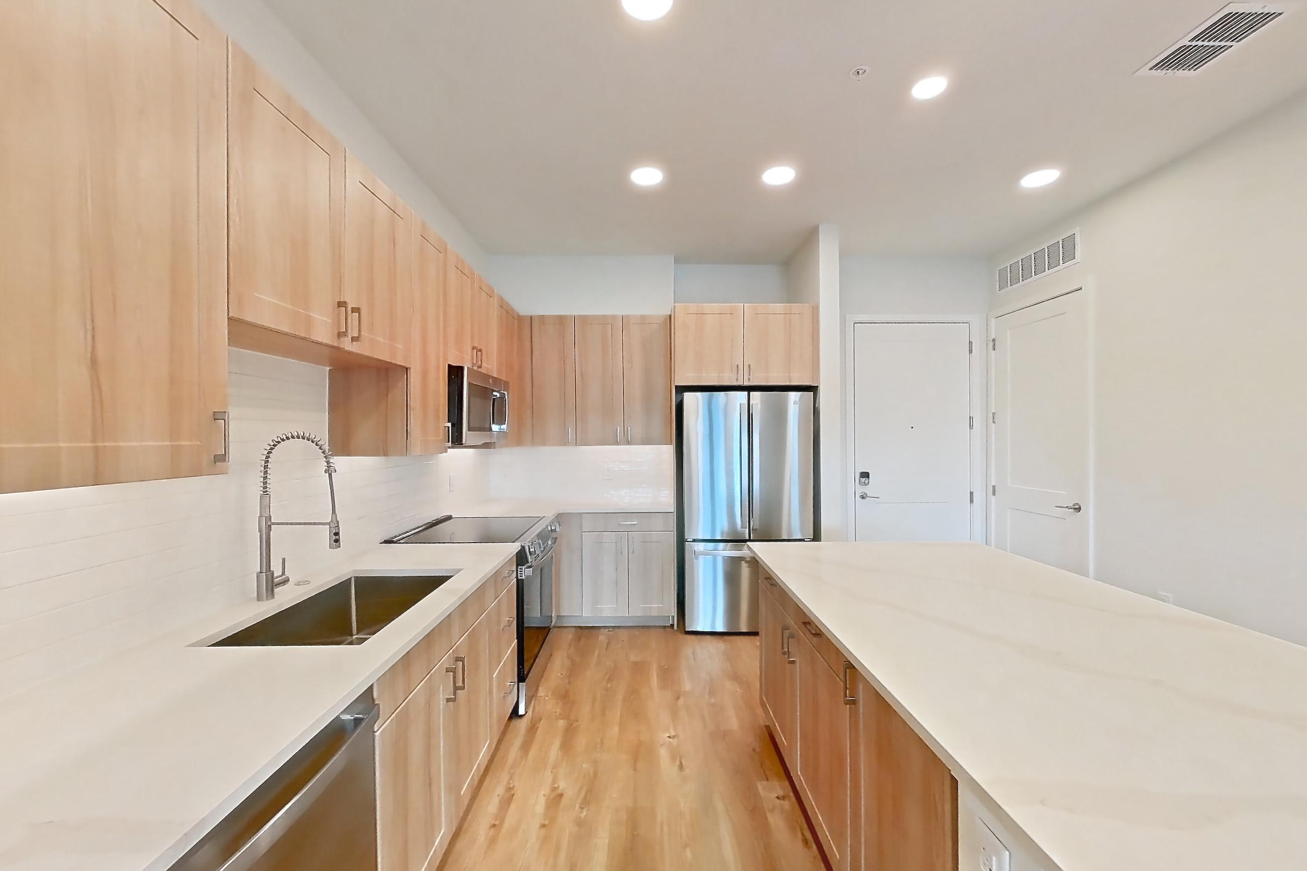 Kitchen with dishwasher, electric range, light stone countertops, light wood-finish flooring, microwave, oven/range, refrigerator, and stainless steel appliances, Apartment 450 at Lantower Bayside