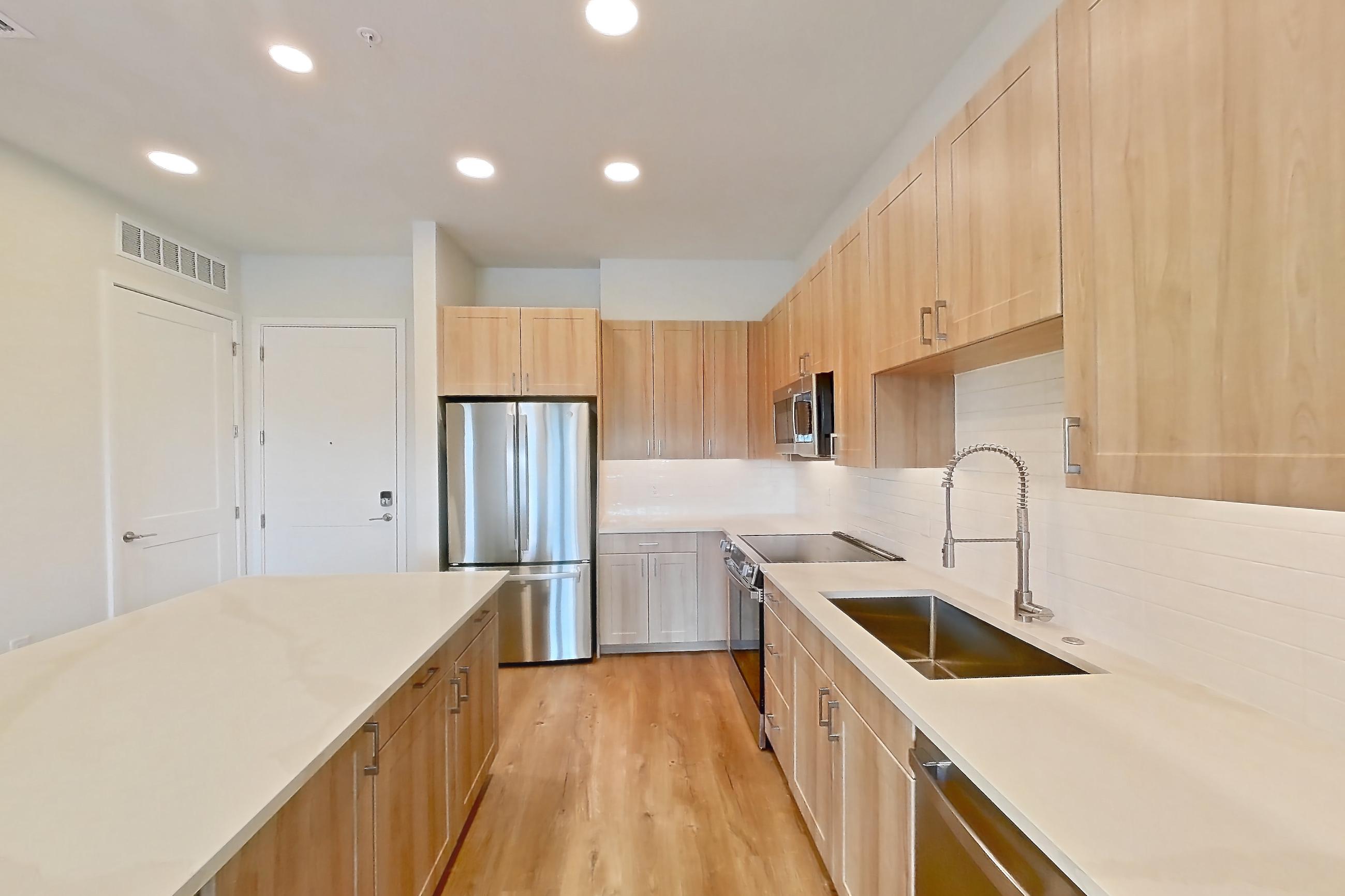 Kitchen with dishwasher, electric range, light countertops, light stone countertops, light wood-finish flooring, microwave, oven/range, refrigerator, and stainless steel appliances, Apartment 452 at Lantower Bayside
