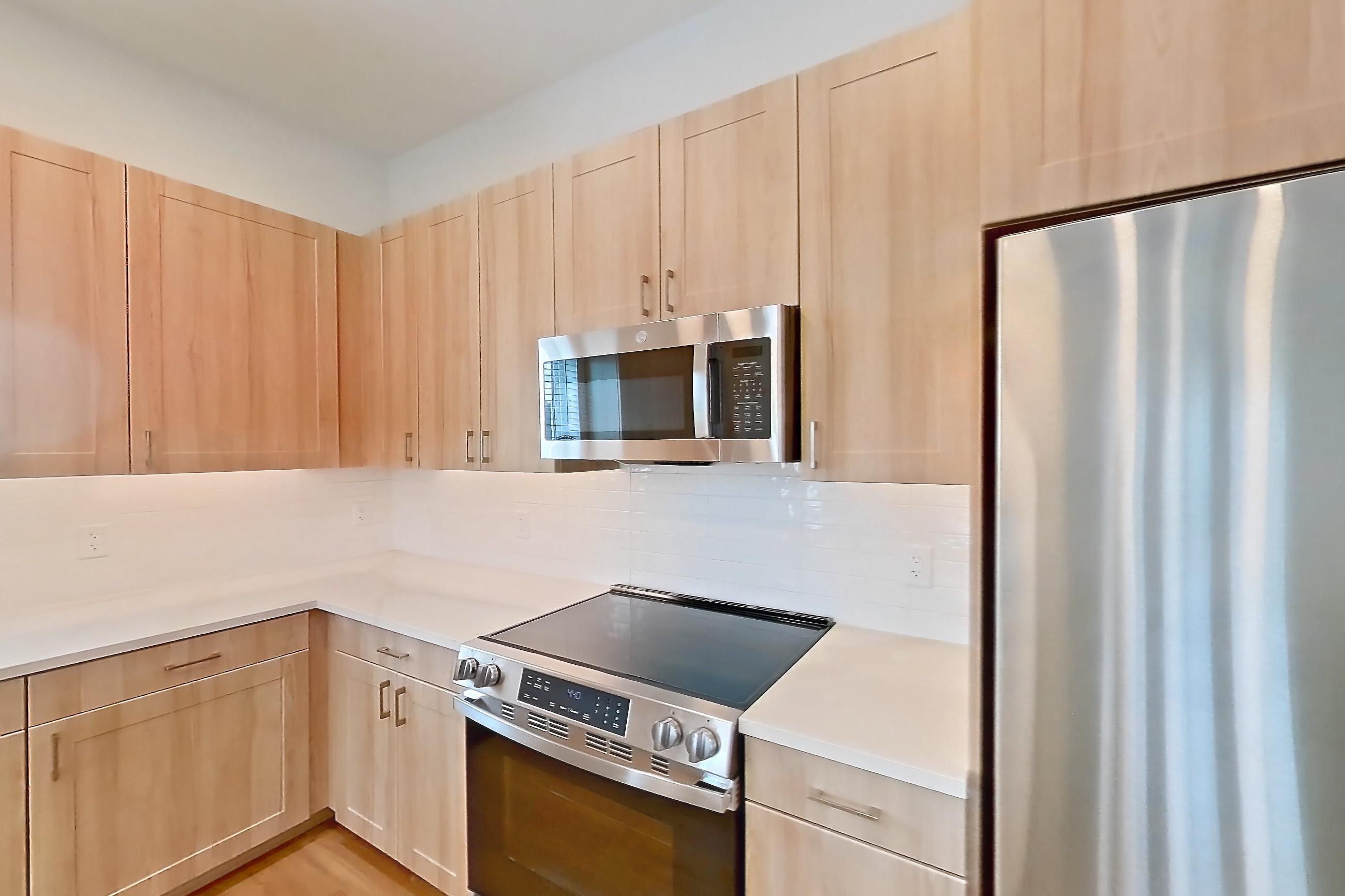 Kitchen with dishwasher, electric range, light countertops, light wood-finish flooring, microwave, oven/range, refrigerator, and stainless steel appliances, Apartment 453 at Lantower Bayside