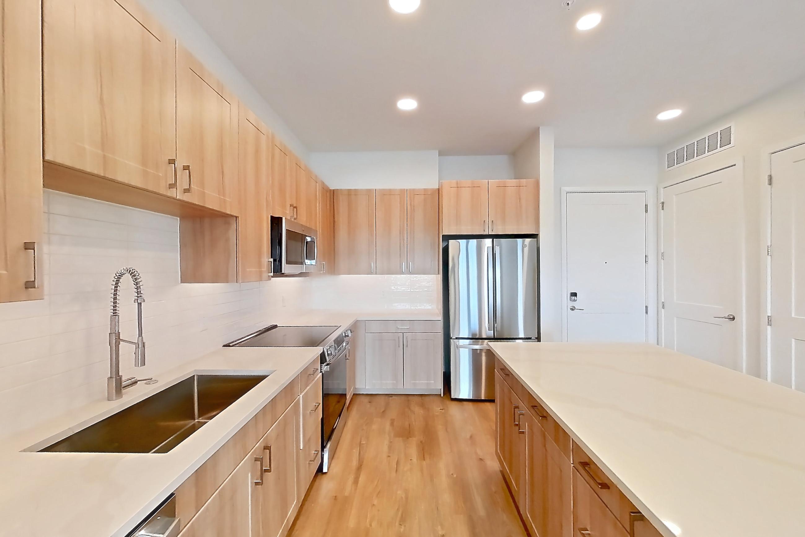 Kitchen with dishwasher, electric range, light countertops, light stone countertops, light wood-finish flooring, oven/range, refrigerator, and stainless steel appliances, Apartment 455 at Lantower Bayside