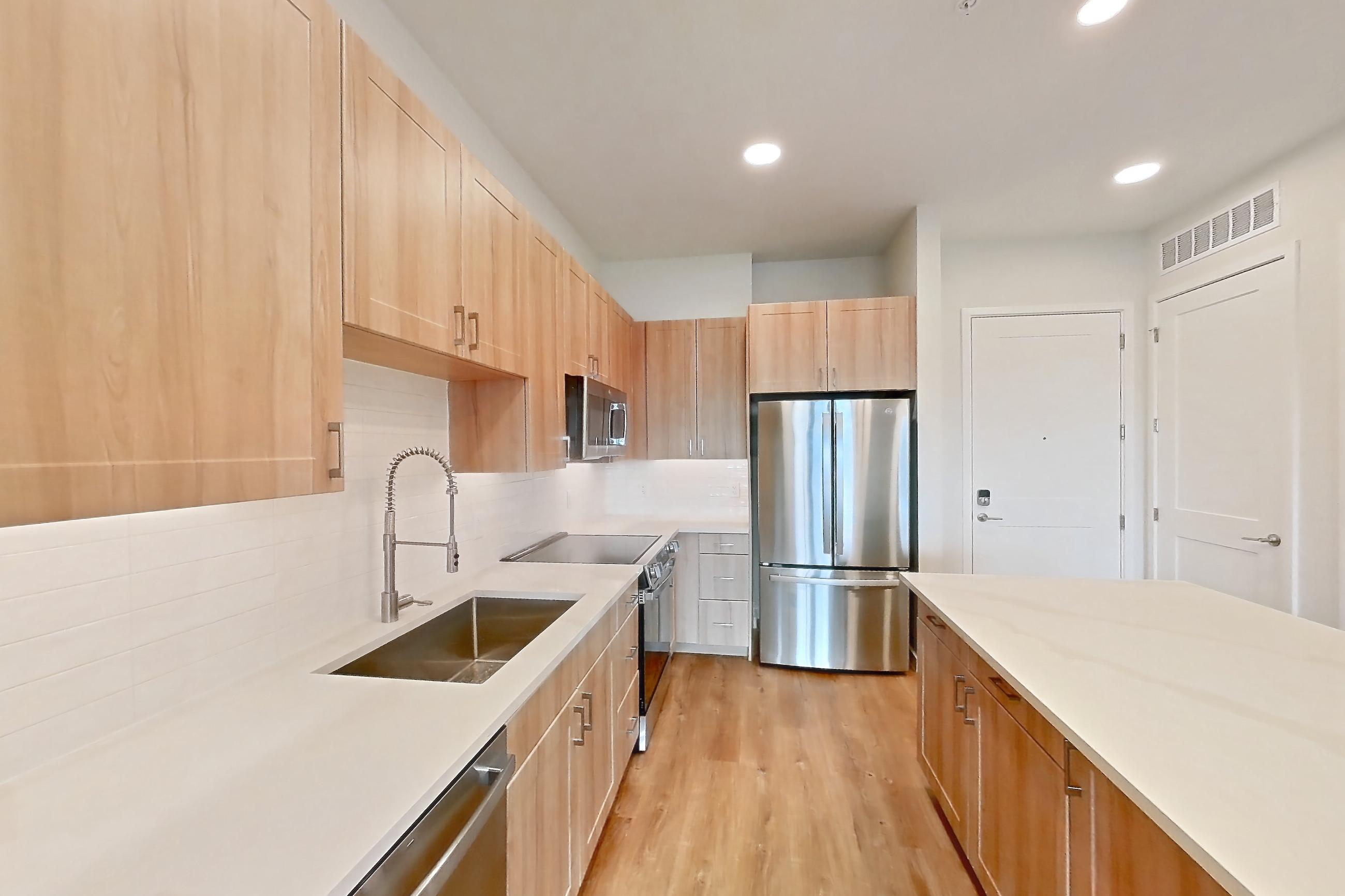 Kitchen with dishwasher, electric range, light countertops, light stone countertops, light wood-finish flooring, microwave, oven/range, refrigerator, and stainless steel appliances, Apartment 457 at Lantower Bayside