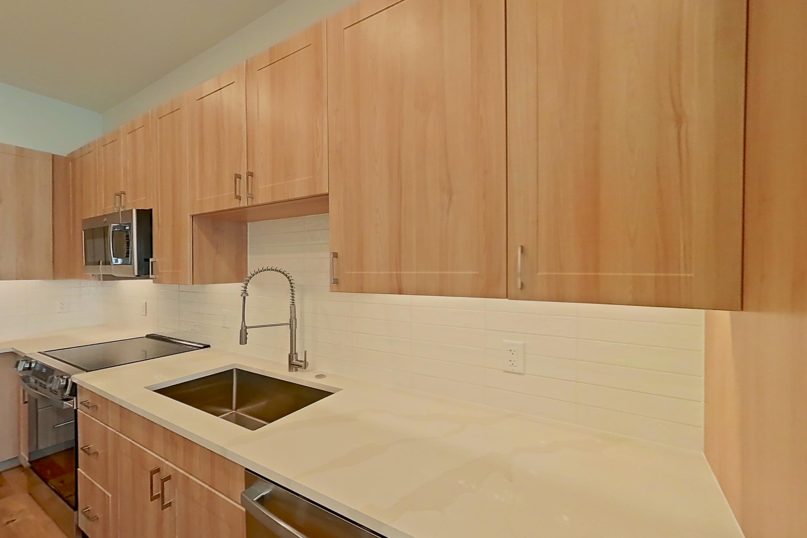 Kitchen with dishwasher, electric range, light countertops, light stone countertops, light wood-finish flooring, microwave, oven/range, refrigerator, and stainless steel appliances, Apartment 458 at Lantower Bayside