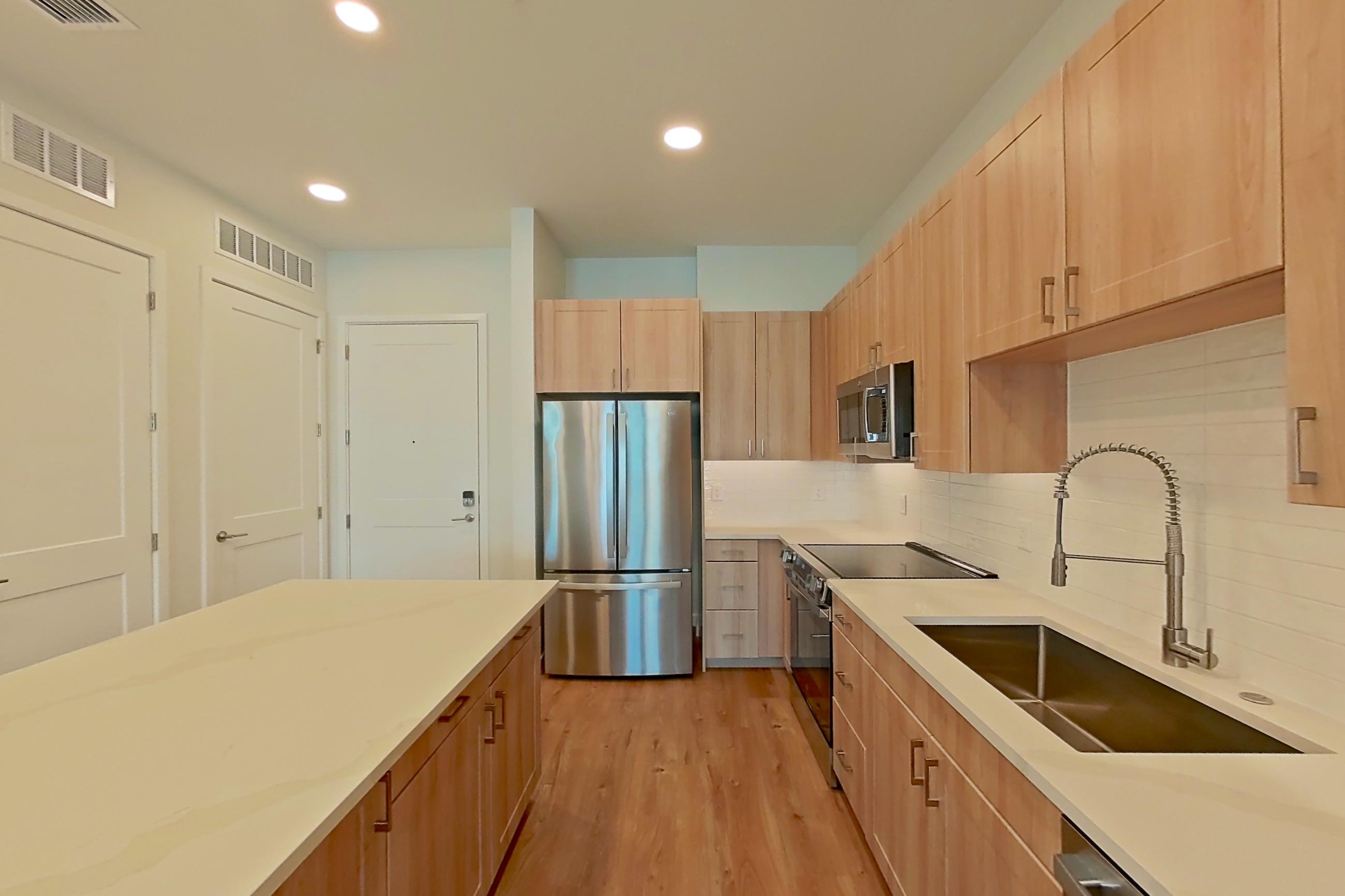 Kitchen with dishwasher, electric range, light countertops, light stone countertops, light wood-finish flooring, microwave, oven/range, refrigerator, and stainless steel appliances, Apartment 458 at Lantower Bayside