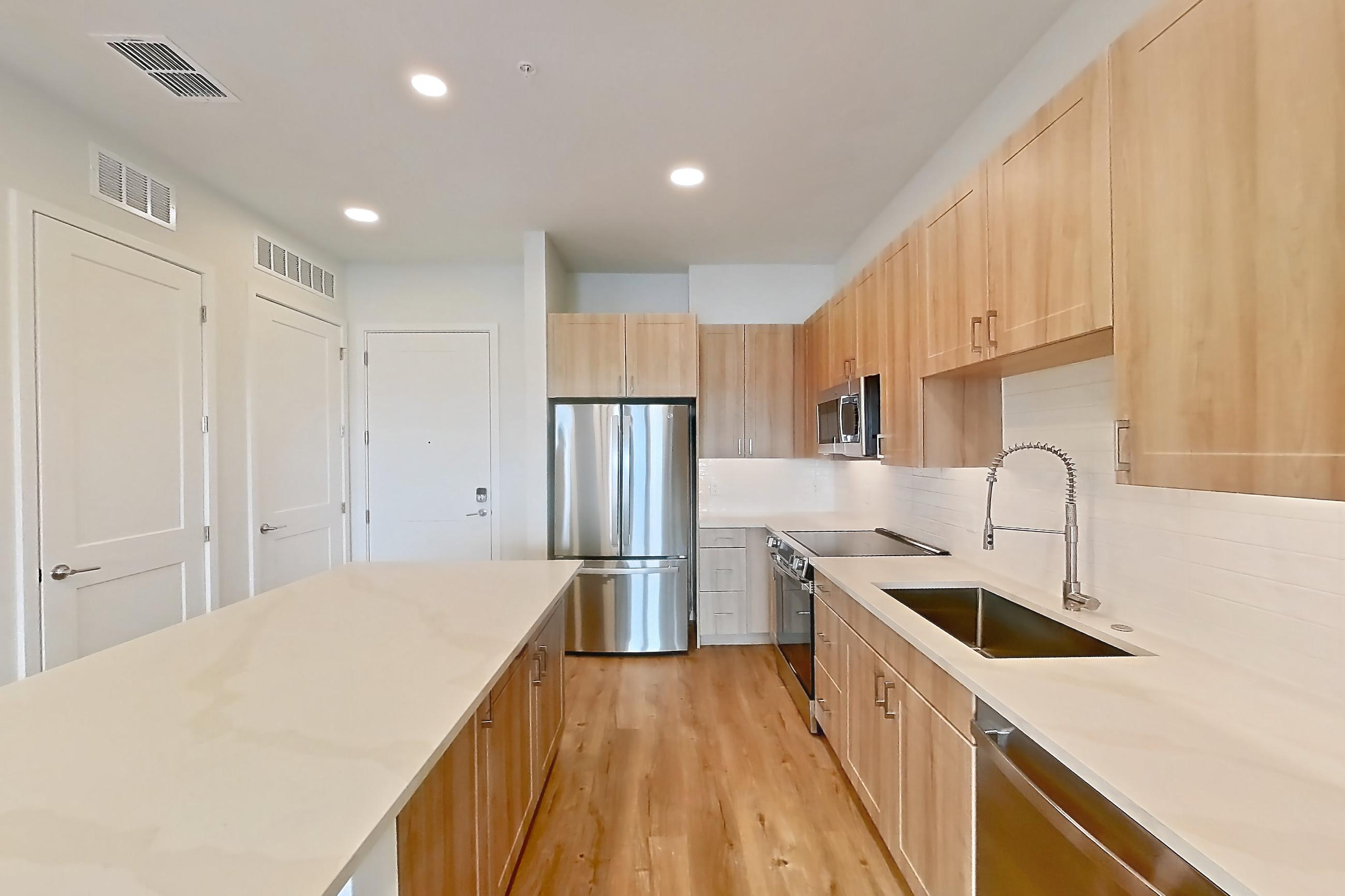 Kitchen with dishwasher, electric range, light countertops, light stone countertops, light wood-finish flooring, microwave, oven/range, refrigerator, and stainless steel appliances, Apartment 459 at Lantower Bayside