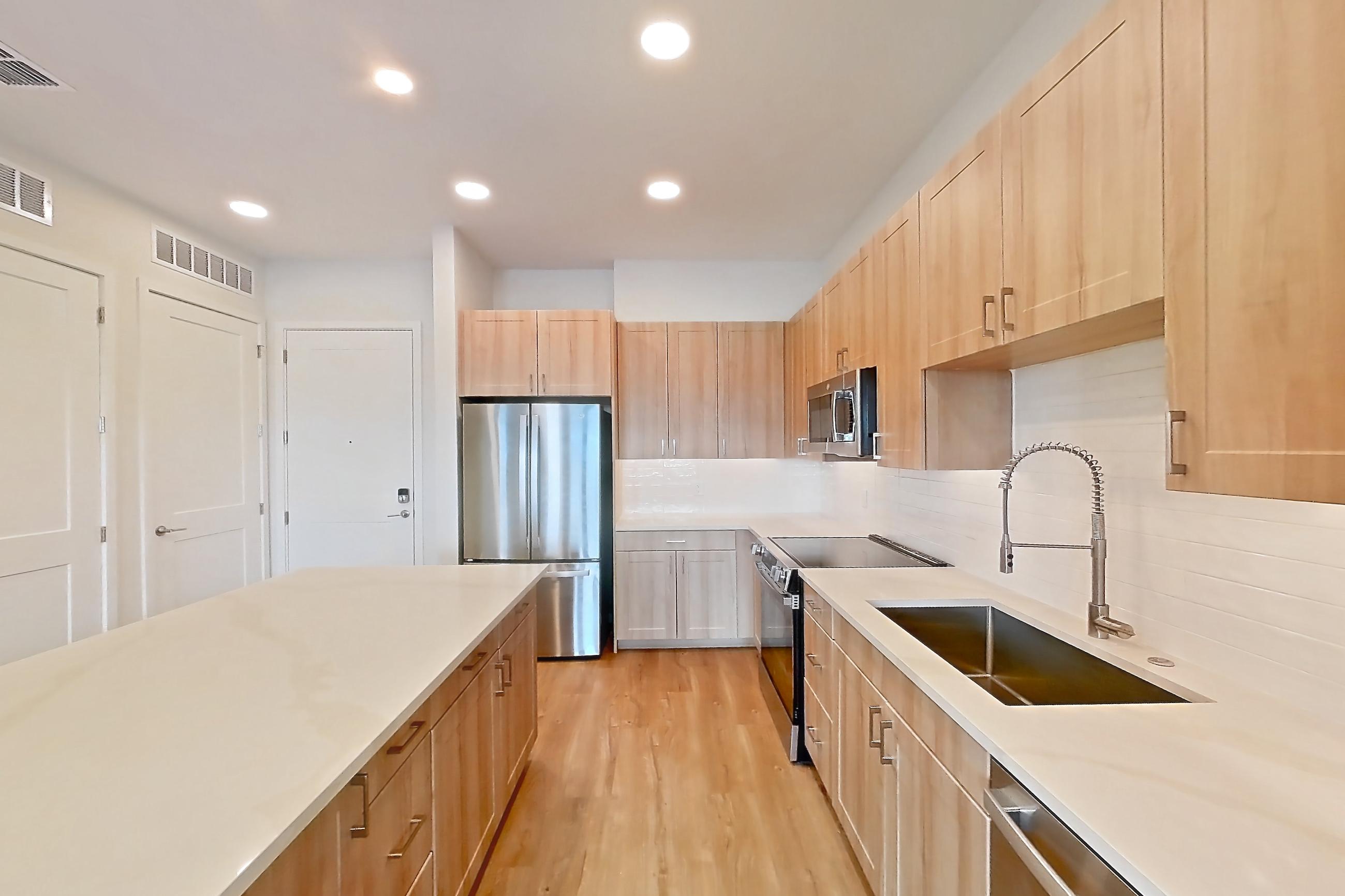 Kitchen with dishwasher, electric range, light countertops, light stone countertops, light wood-finish flooring, microwave, oven/range, refrigerator, and stainless steel appliances, Apartment 463 at Lantower Bayside