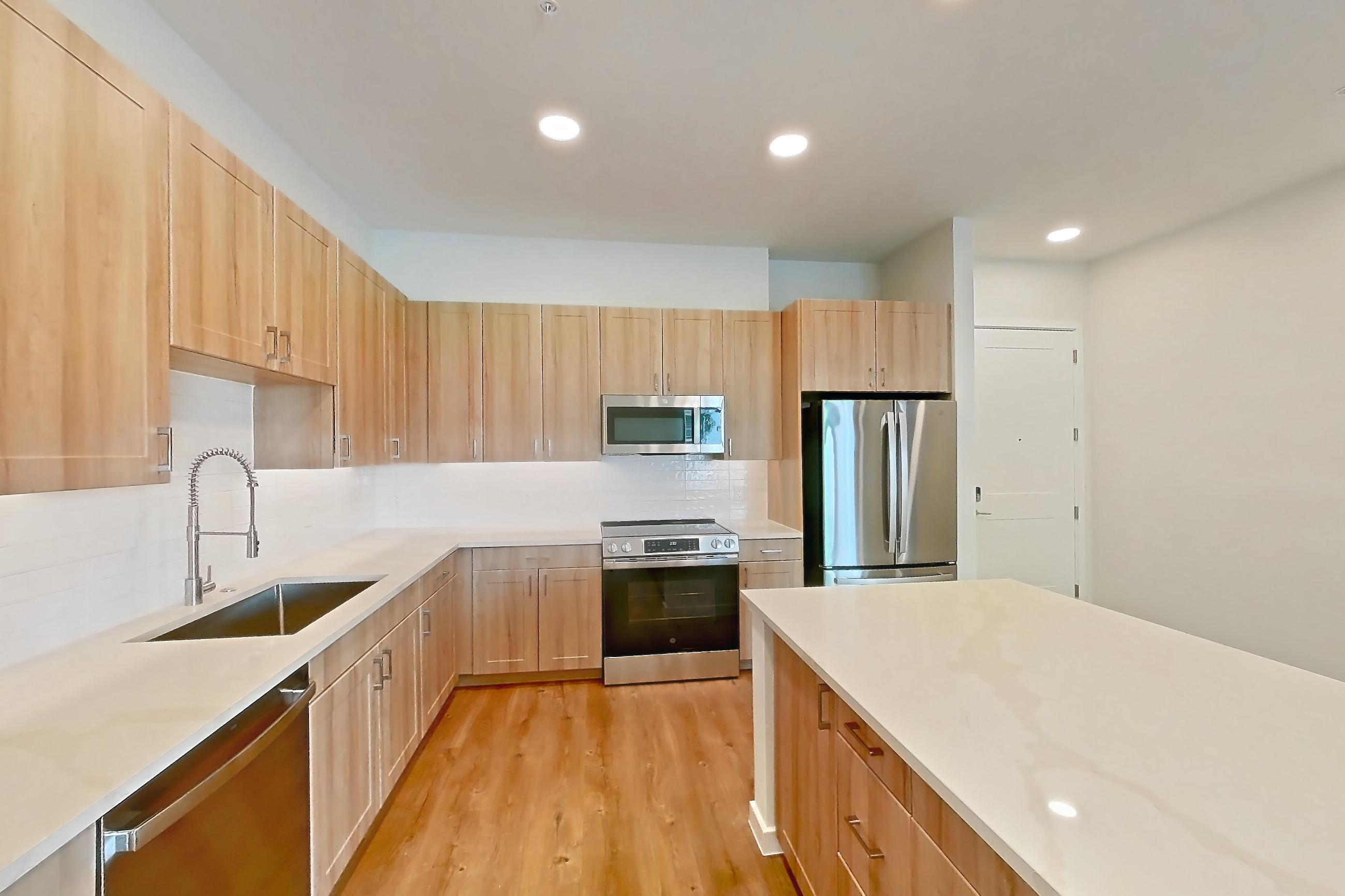 Kitchen with dishwasher, electric range, light stone countertops, light wood-finish flooring, microwave, oven/range, refrigerator, and stainless steel appliances, Apartment 464 at Lantower Bayside