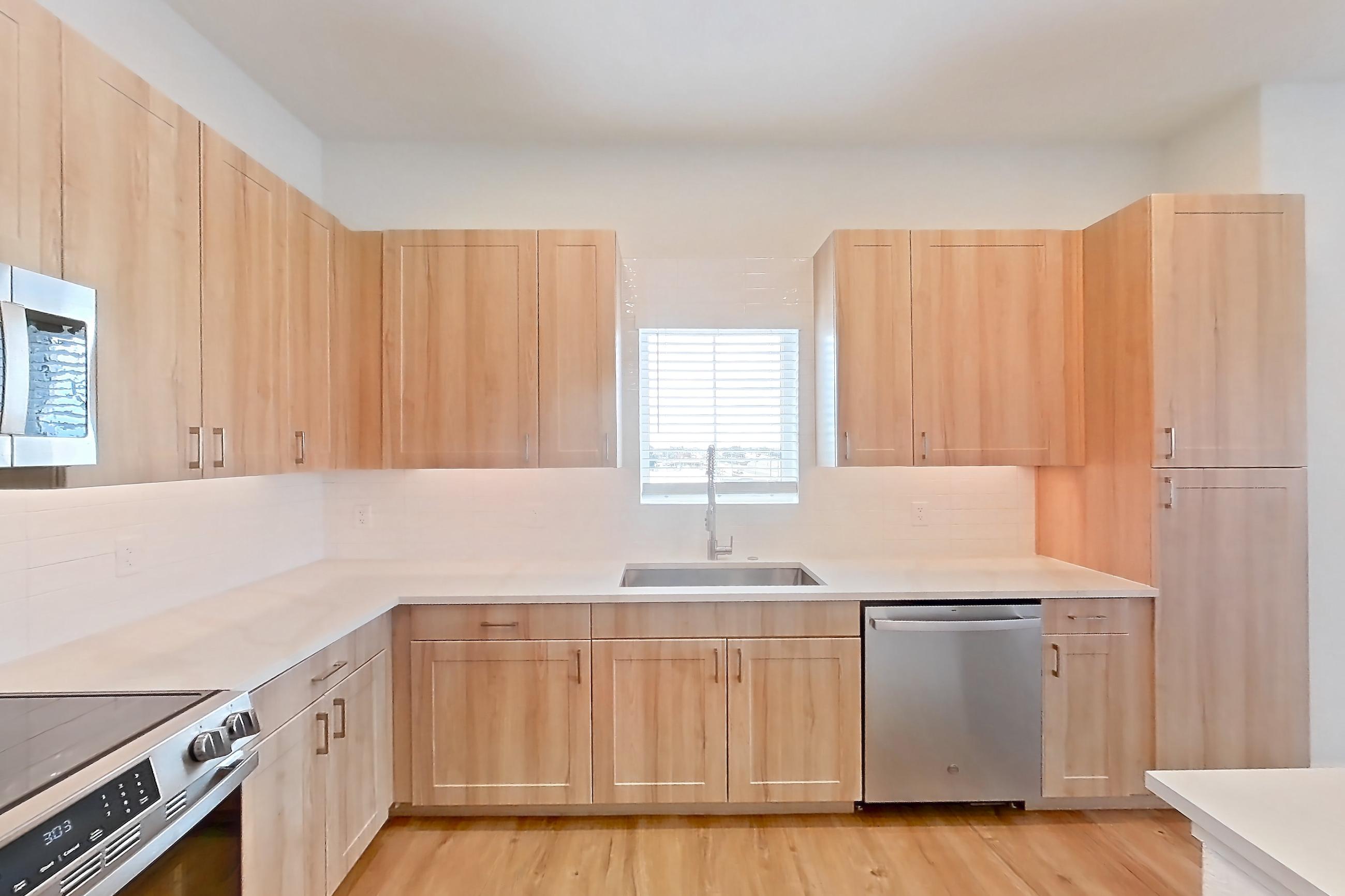 Kitchen with dishwasher, electric range, light countertops, light stone countertops, light wood-finish flooring, microwave, oven/range, refrigerator, and stainless steel appliances, Apartment 465 at Lantower Bayside