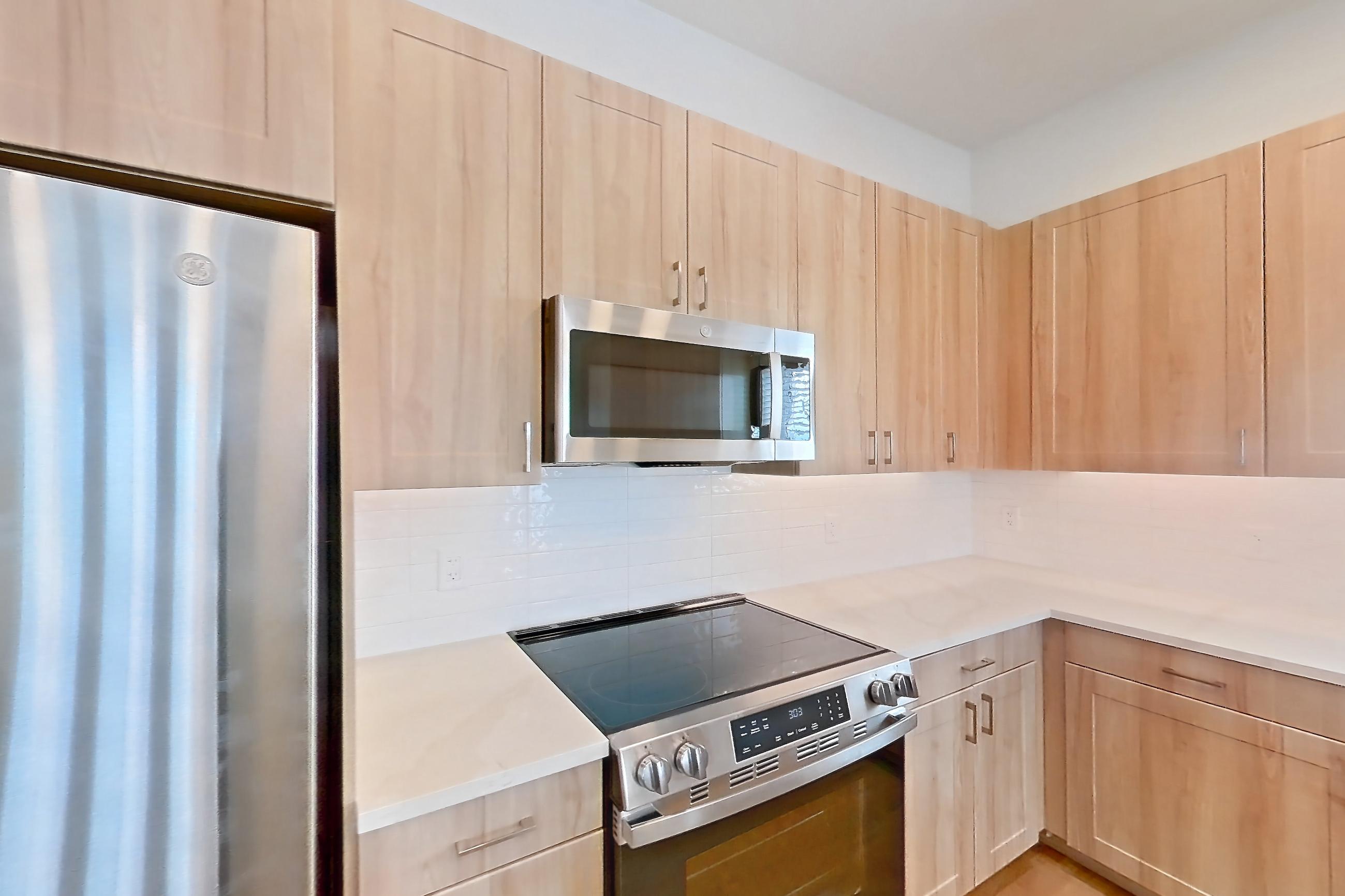 Kitchen with dishwasher, electric range, light countertops, light stone countertops, light wood-finish flooring, microwave, oven/range, refrigerator, and stainless steel appliances, Apartment 465 at Lantower Bayside