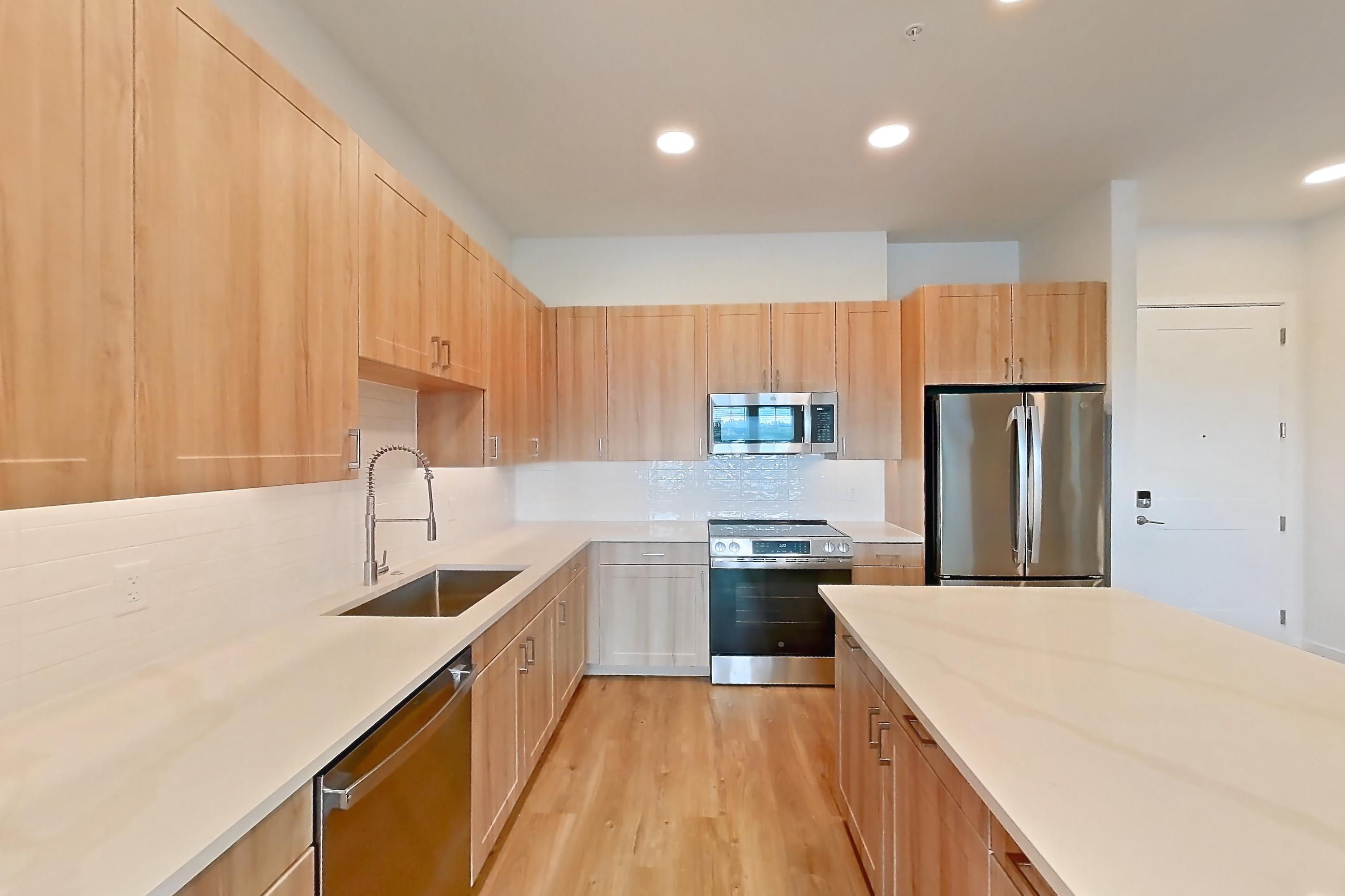 Kitchen with dishwasher, electric range, light countertops, light stone countertops, light wood-finish flooring, microwave, oven/range, refrigerator, and stainless steel appliances, Apartment 466 at Lantower Bayside