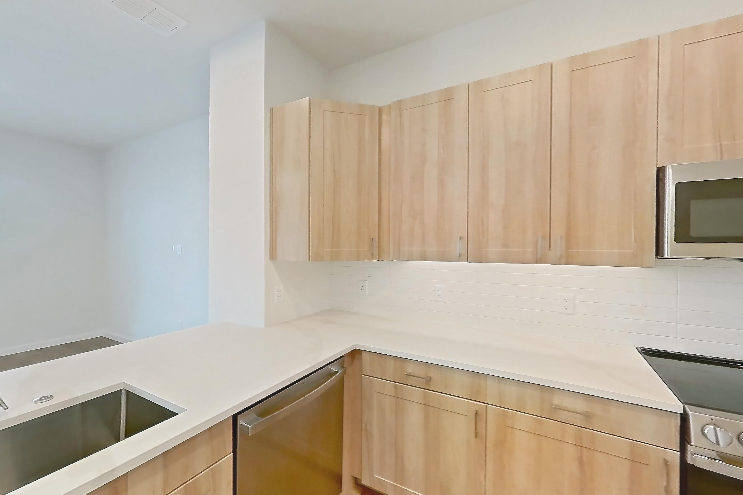 Kitchen with dishwasher, electric range, light countertops, light stone countertops, light wood-finish flooring, microwave, oven/range, and stainless steel appliances, Apartment 470 at Lantower Bayside