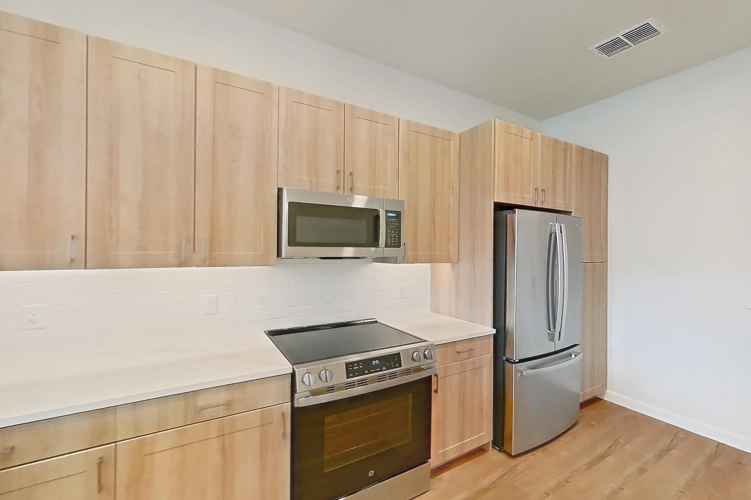 Kitchen with dishwasher, electric range, light countertops, light stone countertops, light wood-finish flooring, microwave, oven/range, and stainless steel appliances, Apartment 470 at Lantower Bayside