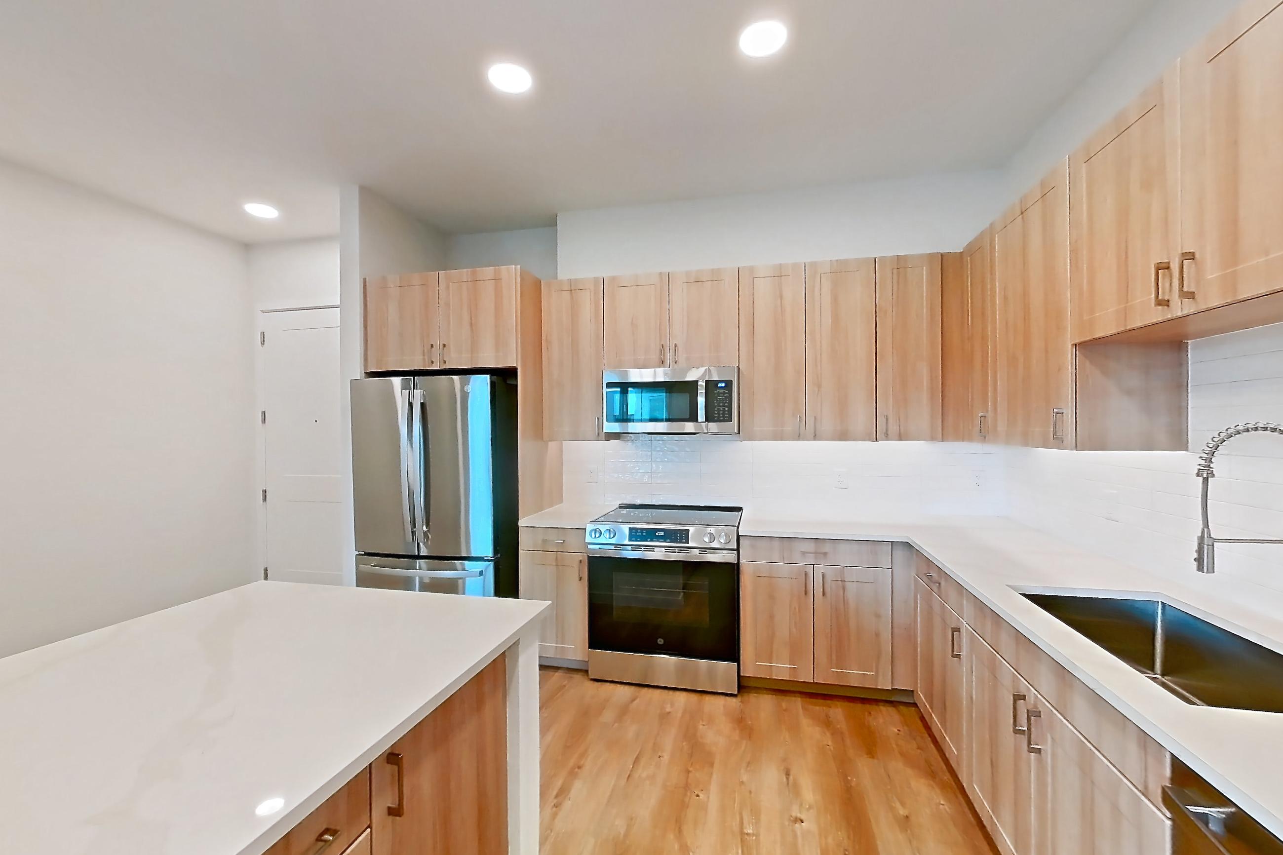 Kitchen with dishwasher, electric range, light countertops, light stone countertops, light wood-finish flooring, microwave, oven/range, refrigerator, and stainless steel appliances, Apartment 474 at Lantower Bayside